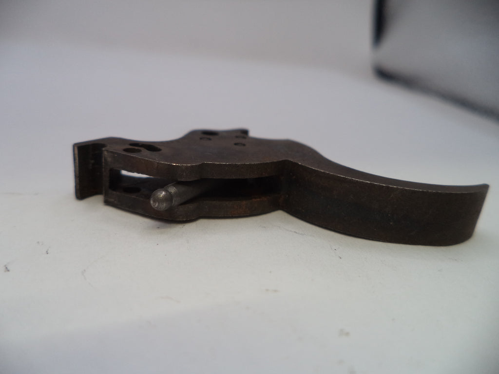 A dark metal trigger assembly, likely for a firearm, resting on a white surface.