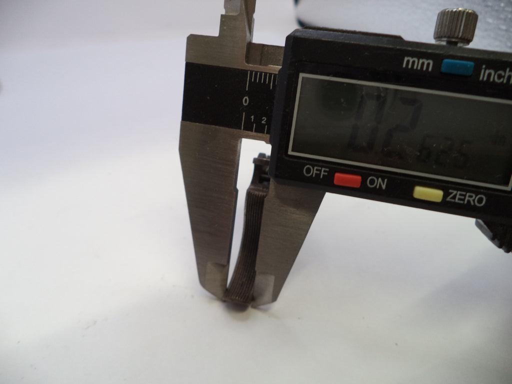 A digital caliper measuring tool with a black display screen and silver metal jaws, shown measuring a small dark object on a plain white surface.