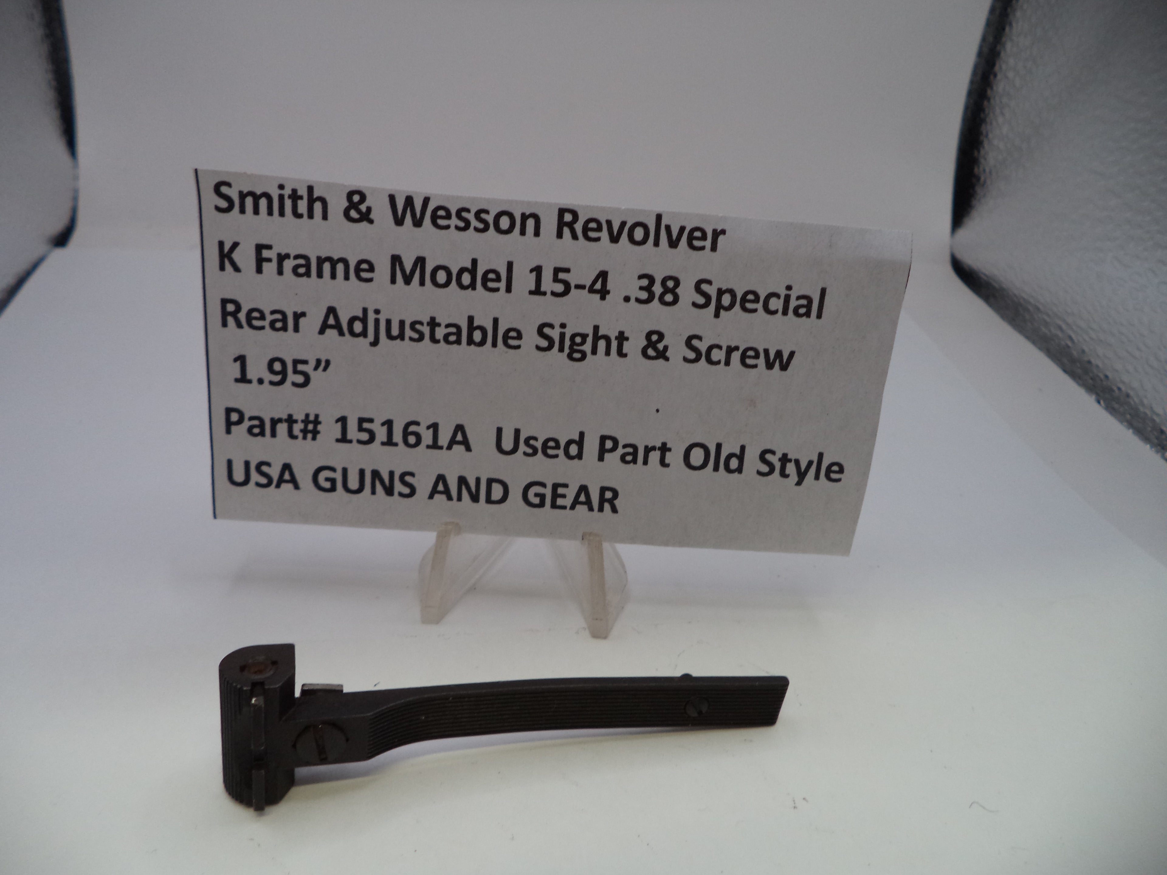 A black metal Smith & Wesson revolver rear adjustable sight and screw part on a white surface, with a paper label card displaying part number 15161A and product details.