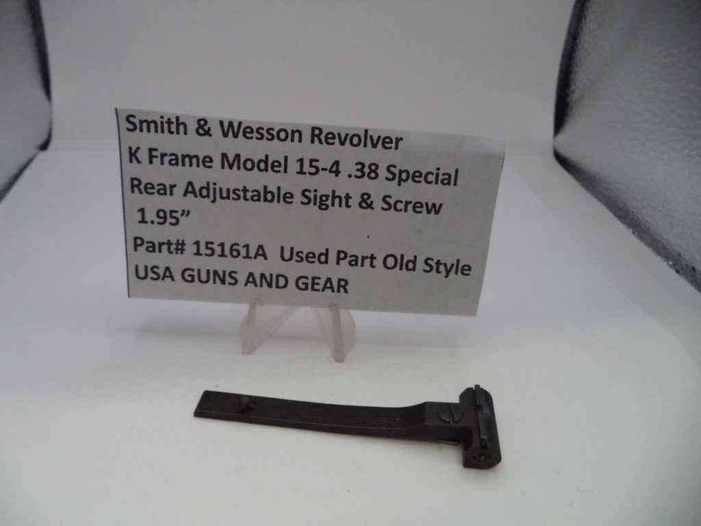 A black metal rear adjustable sight and screw part for a Smith & Wesson revolver, displayed on a white surface with a small clear stand holding a label card.