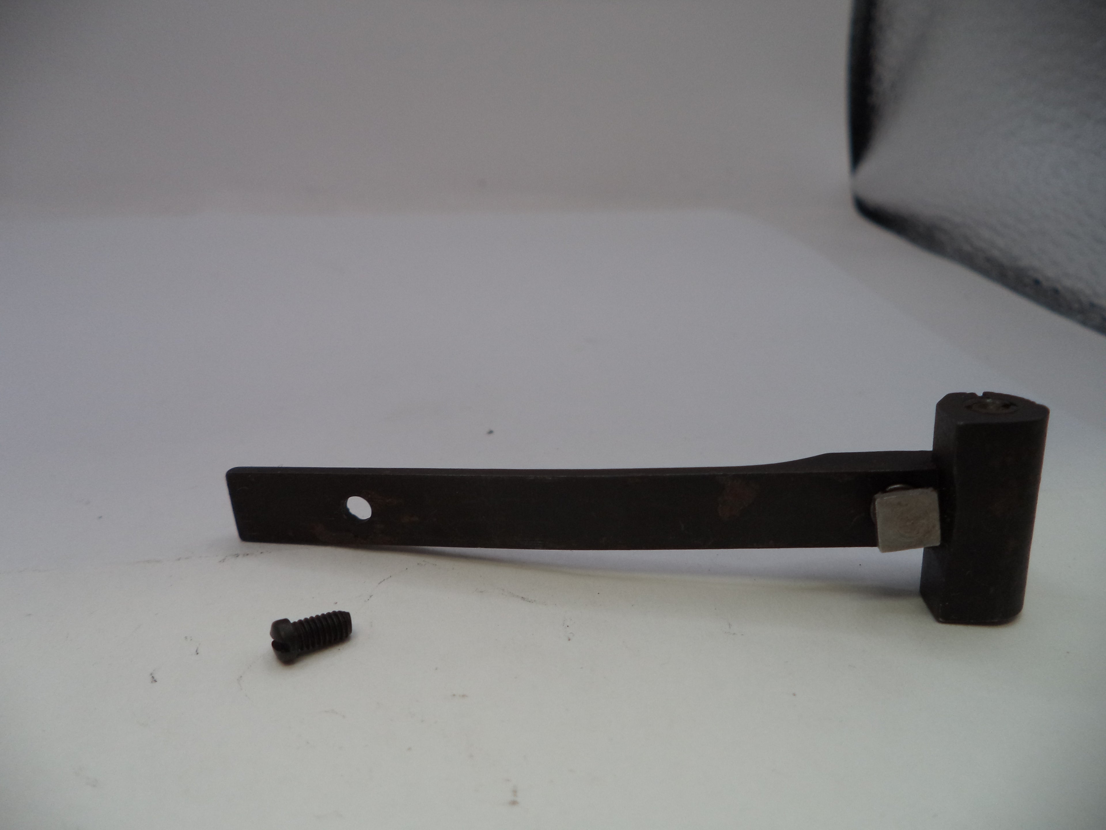 A dark metal lever or bracket with a small screw fastener placed beside it on a plain white surface.