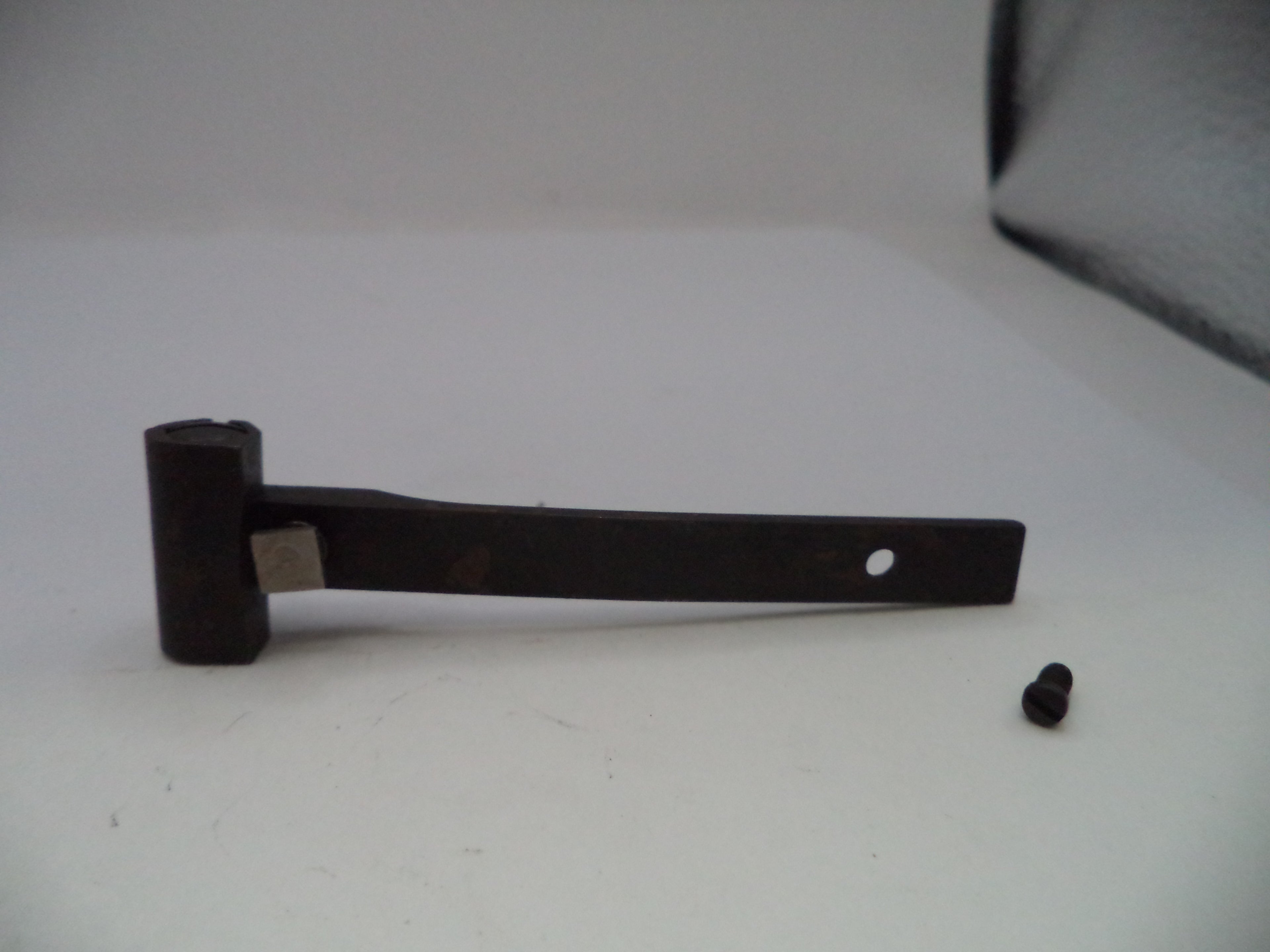 A dark metal hinge or bracket with a small mounting screw placed beside it on a plain light background.