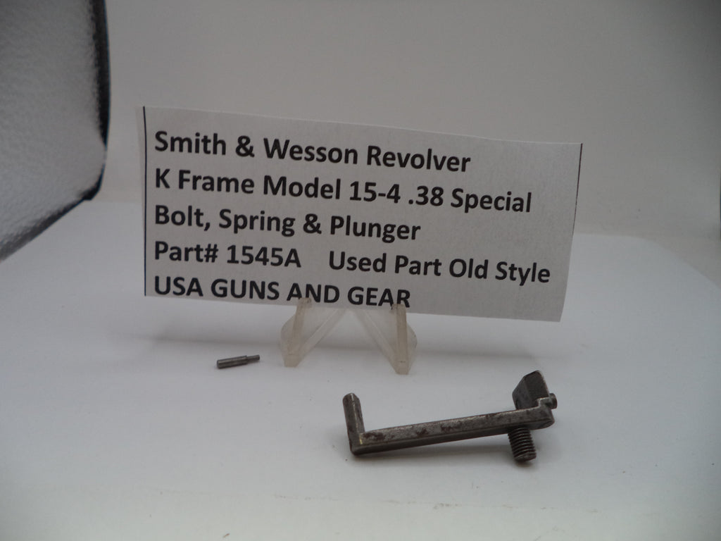 A used metal bolt, spring, and plunger part for a Smith & Wesson revolver, displayed on a white surface with a small sign identifying the part and model.