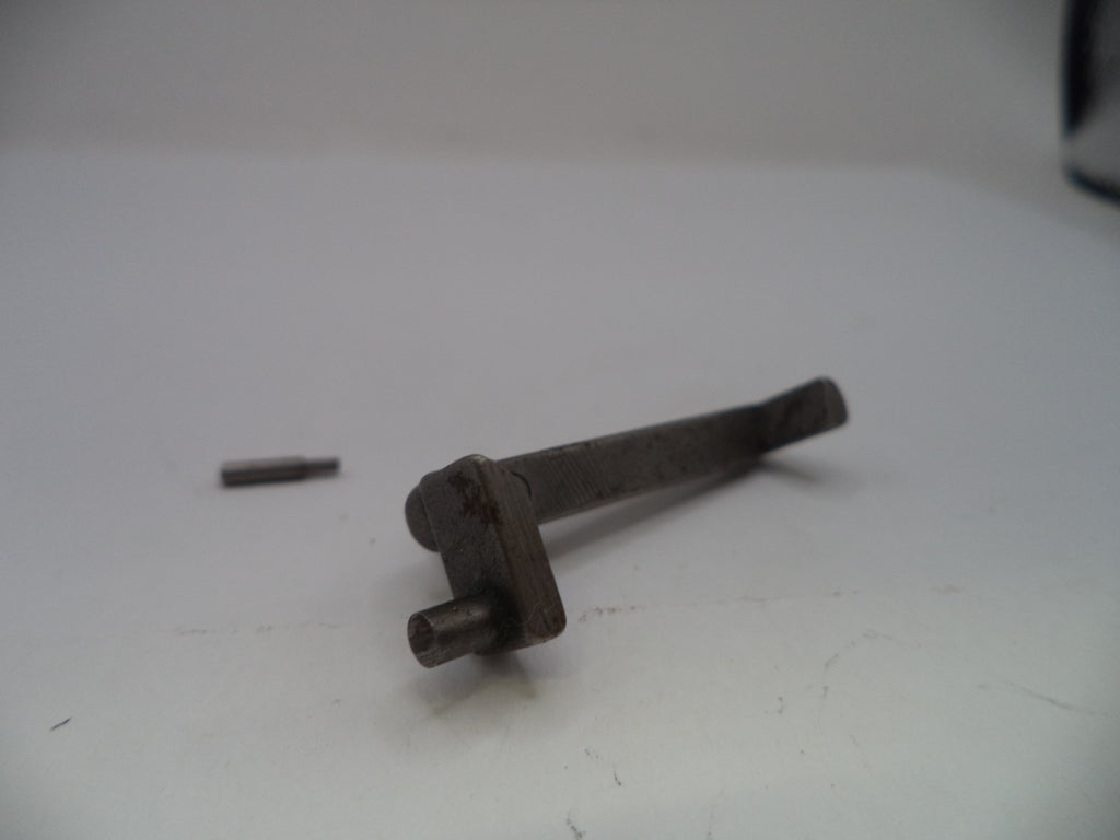 A small dark metal mechanical part or tool component with a short cylindrical pin and a bent stem, photographed on a plain light background with a separate small pin nearby.