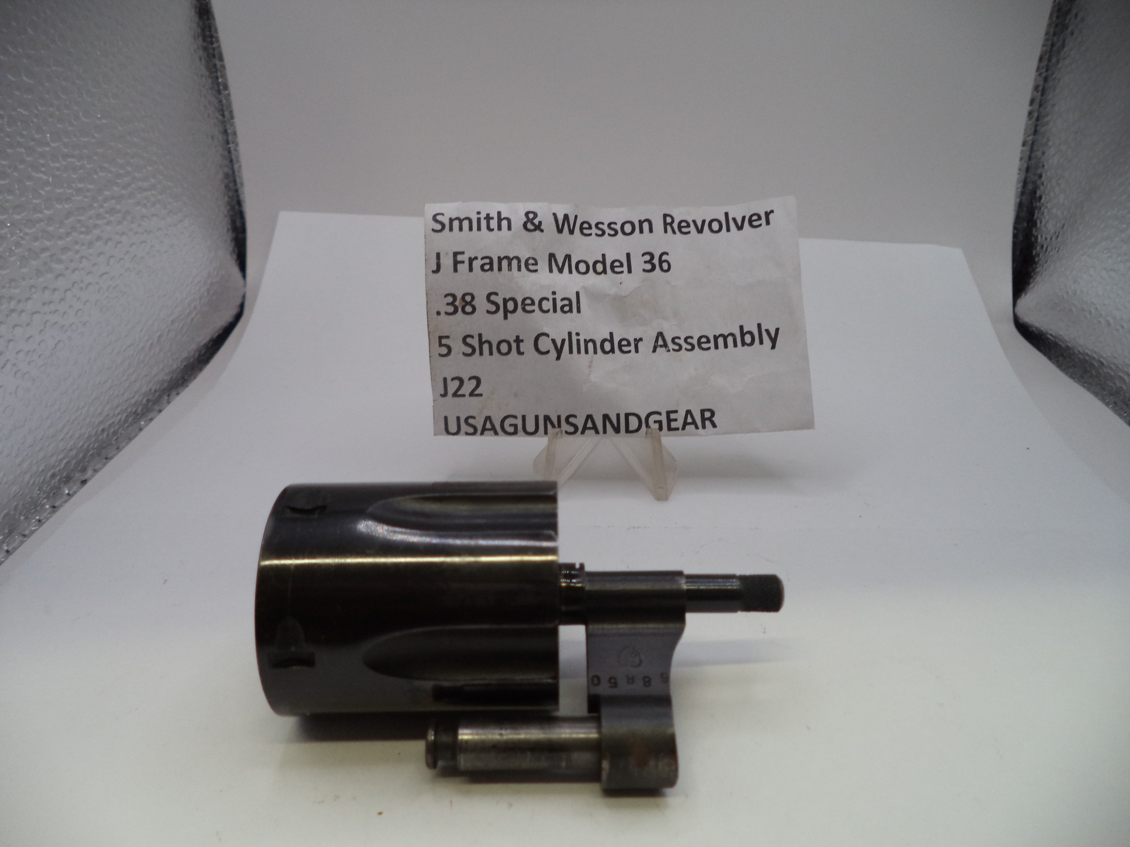 A Smith & Wesson revolver J frame model 36 .38 special 5 shot cylinder assembly, displayed on a white surface with a small paper label card in the background.