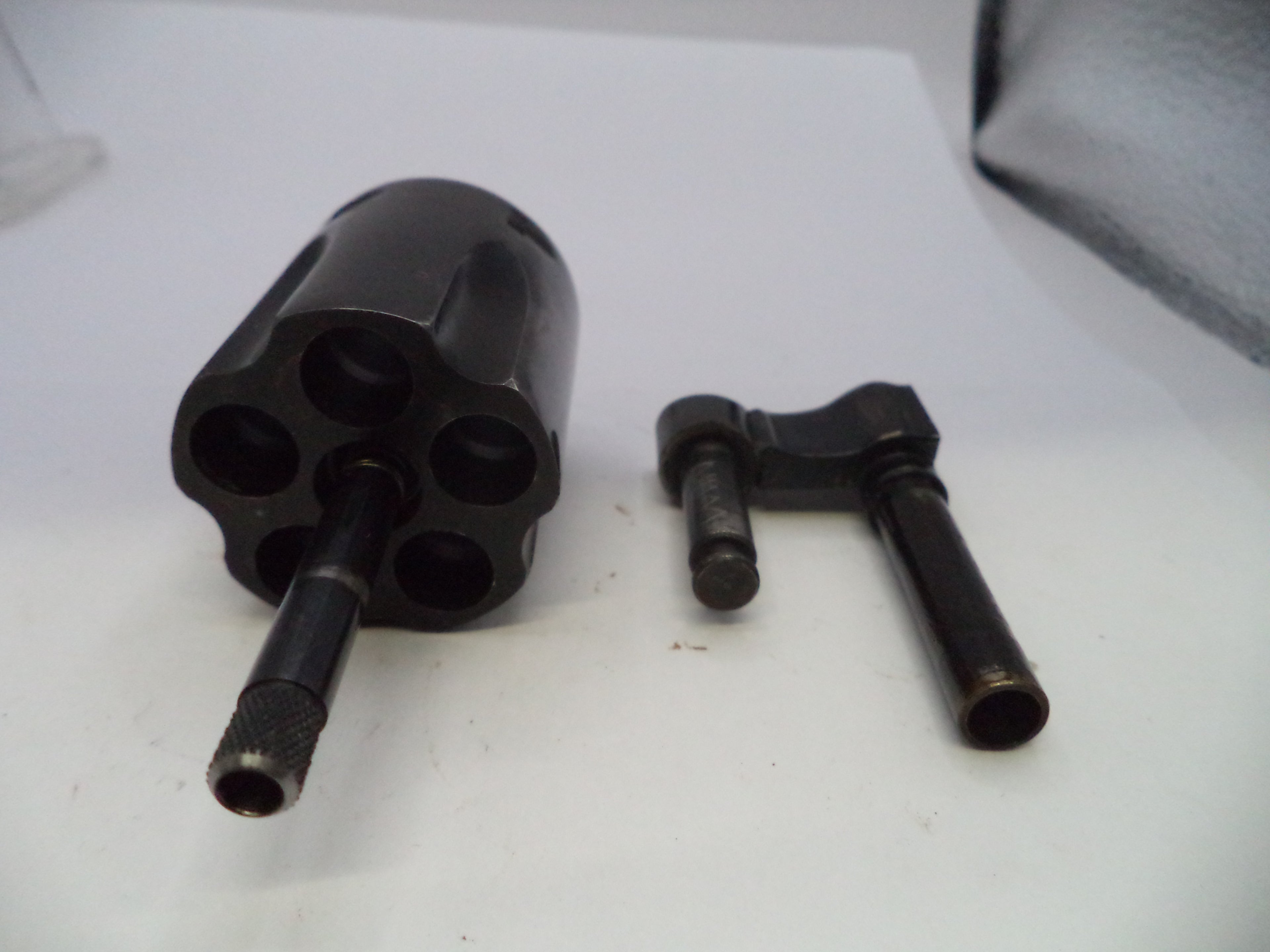 A black metal revolver cylinder and a black metal barrel sleeve or adapter, shown as a set on a plain white surface.