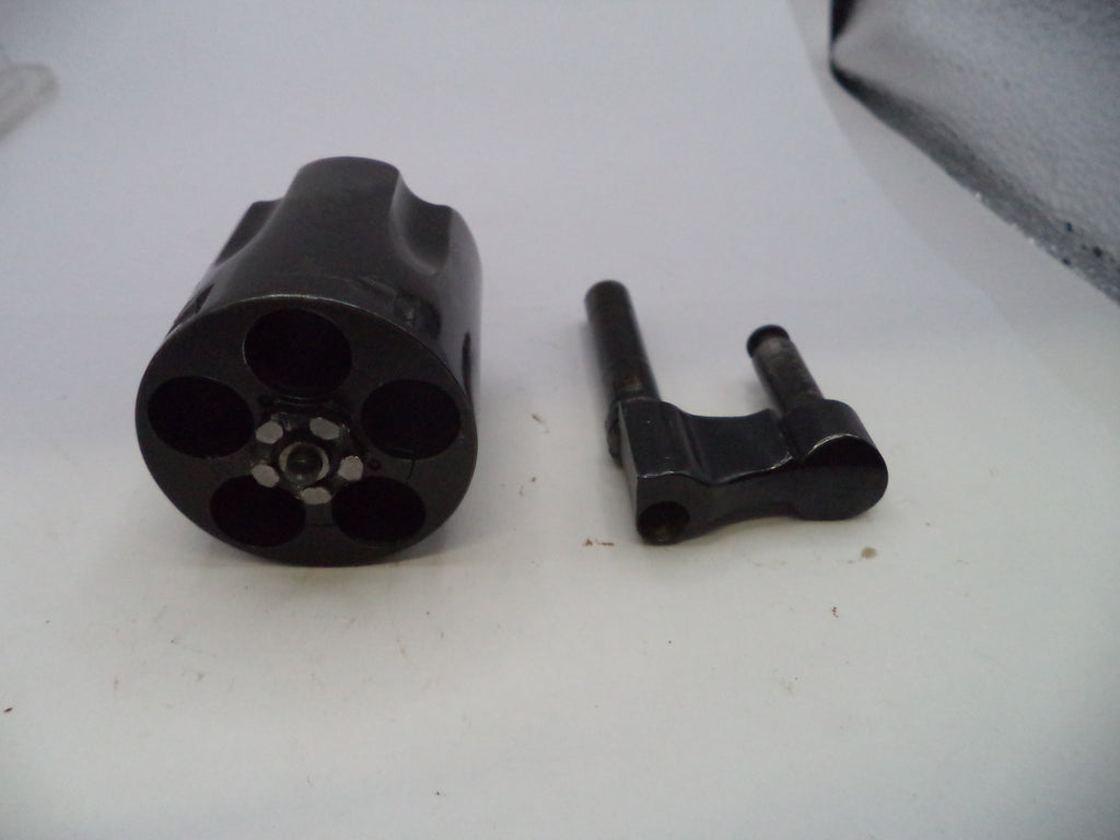 A black metal revolver cylinder and a matching black metal bolt carrier assembly placed side by side on a white surface.