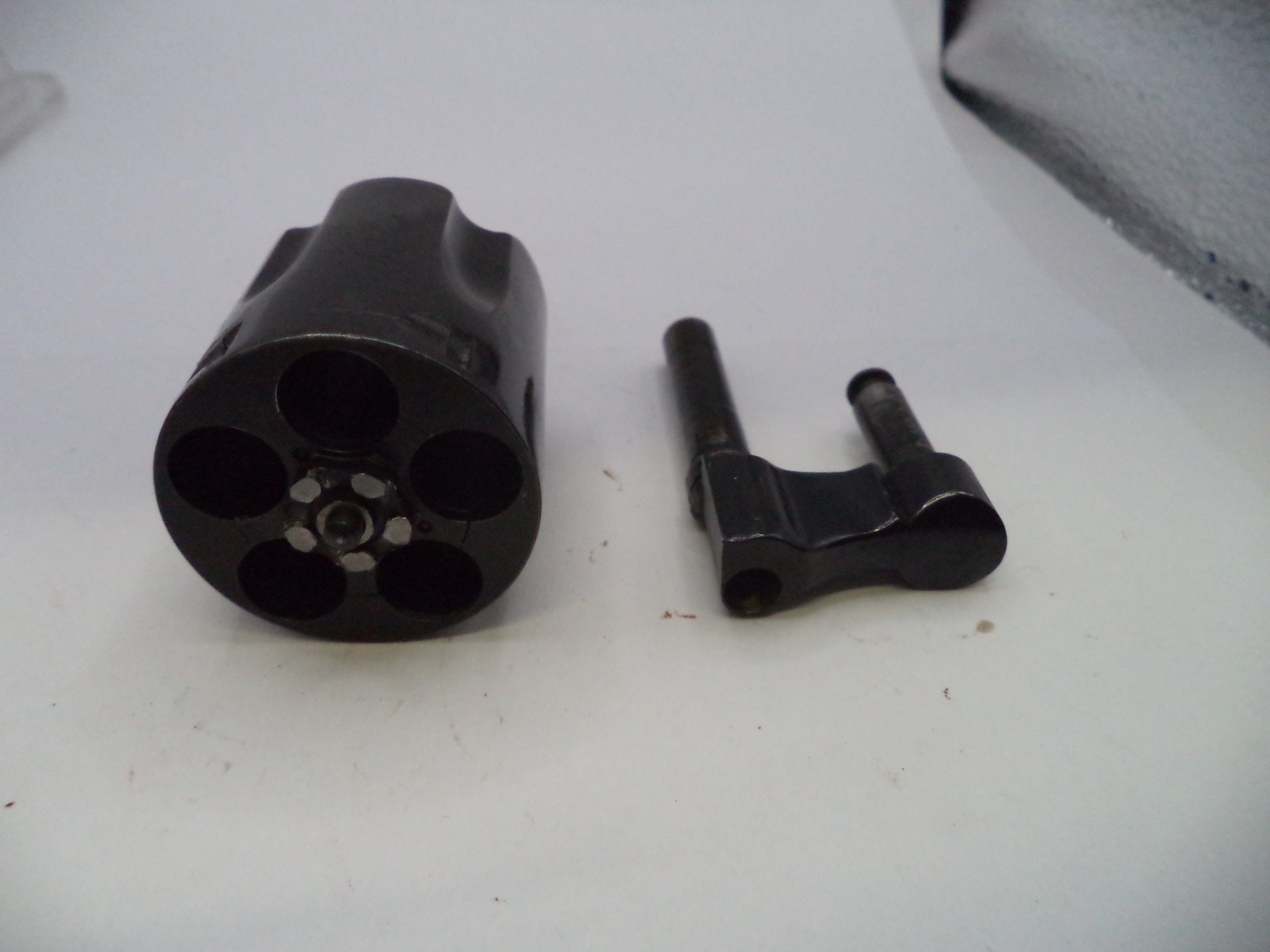 A black metal revolver cylinder and a matching black metal bolt carrier assembly placed side by side on a white surface.