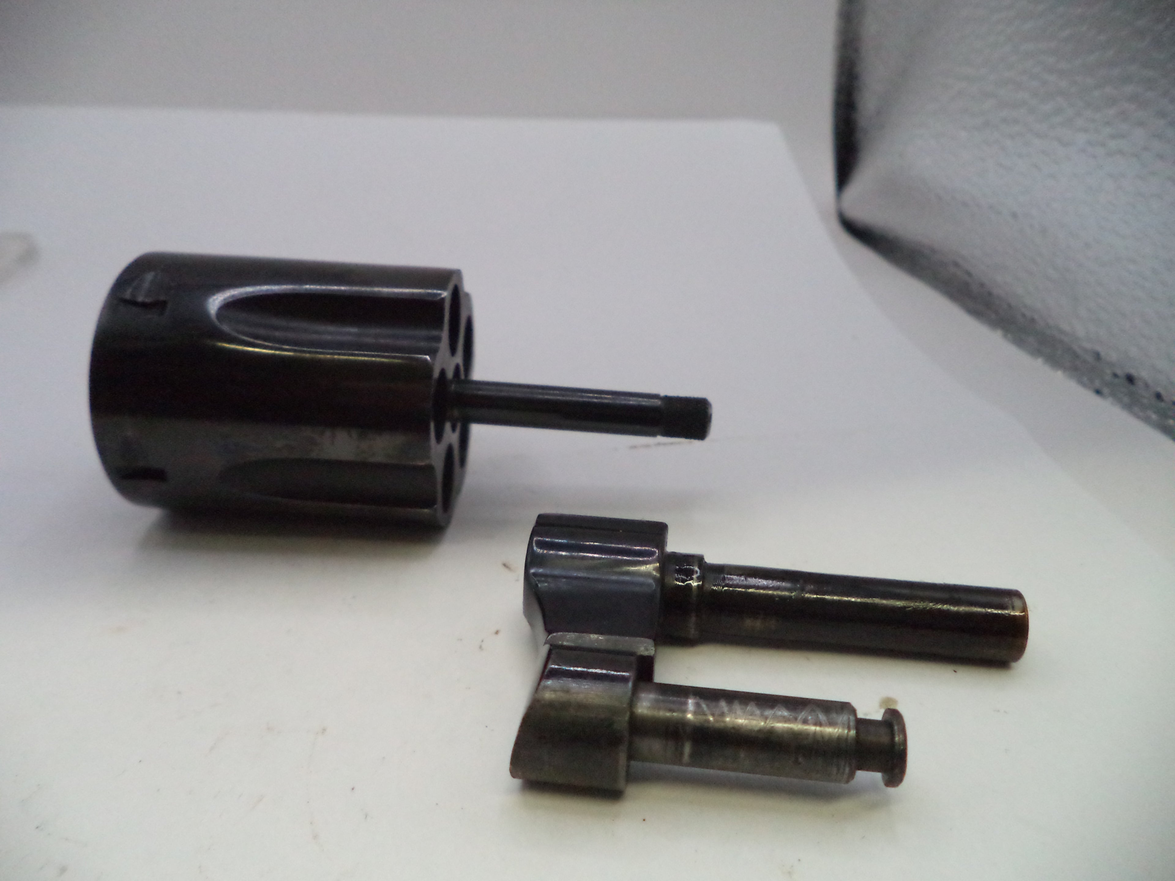 A black metal revolver cylinder and two matching barrel shims or pins displayed on a white surface.