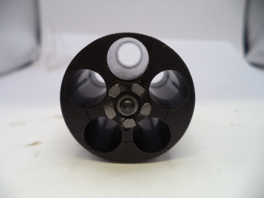 A close-up of a black circular metal component with five circular openings, photographed on a white surface with a soft-focus light gray background.