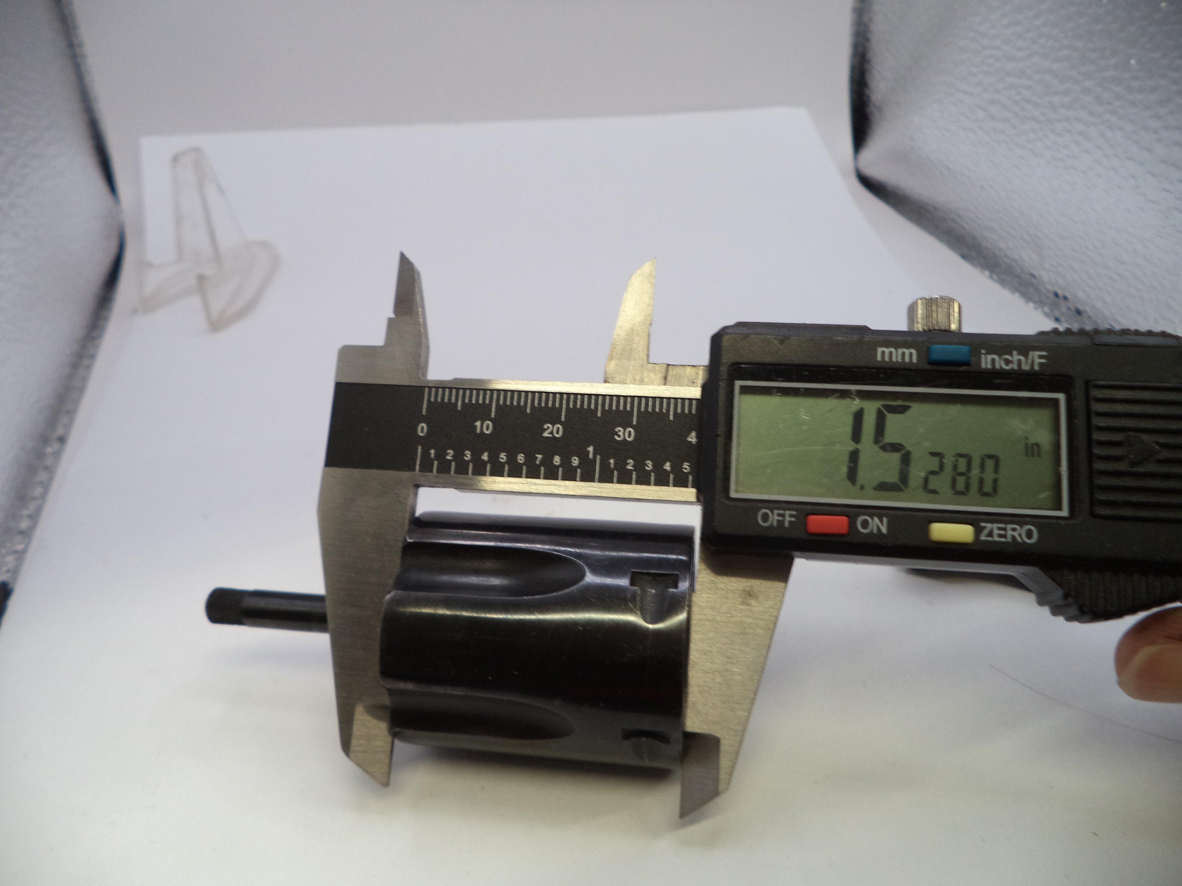 A black cylindrical component being measured with a digital caliper, showing a width reading of 15.280 inches (388.