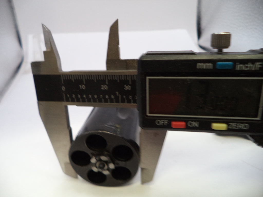 A digital caliper measuring the diameter of a black cylindrical object with four circular holes, shown on a white surface.