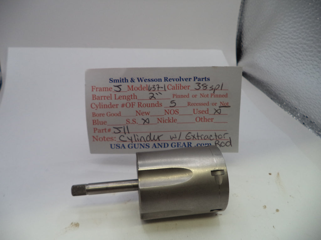 A used metal revolver cylinder and extractor assembly from Smith & Wesson, shown with its original handwritten parts identification card on a white surface.