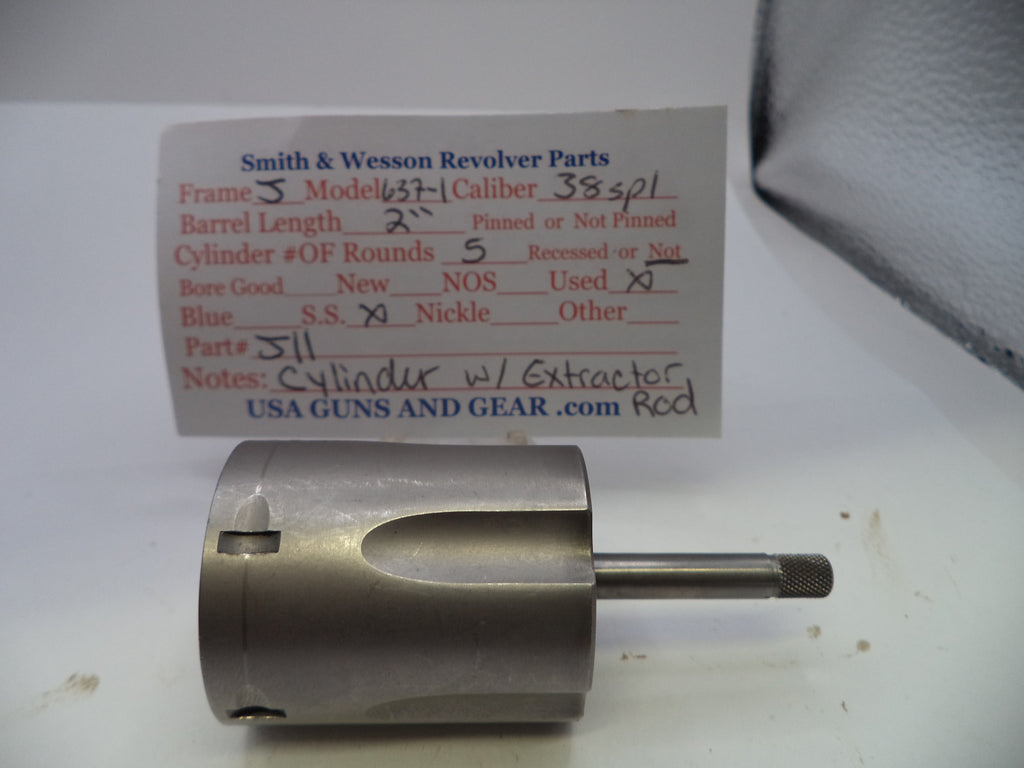 A metal revolver cylinder and extractor assembly placed on a white surface in front of a handwritten parts label card for Smith & Wesson Revolver Parts.