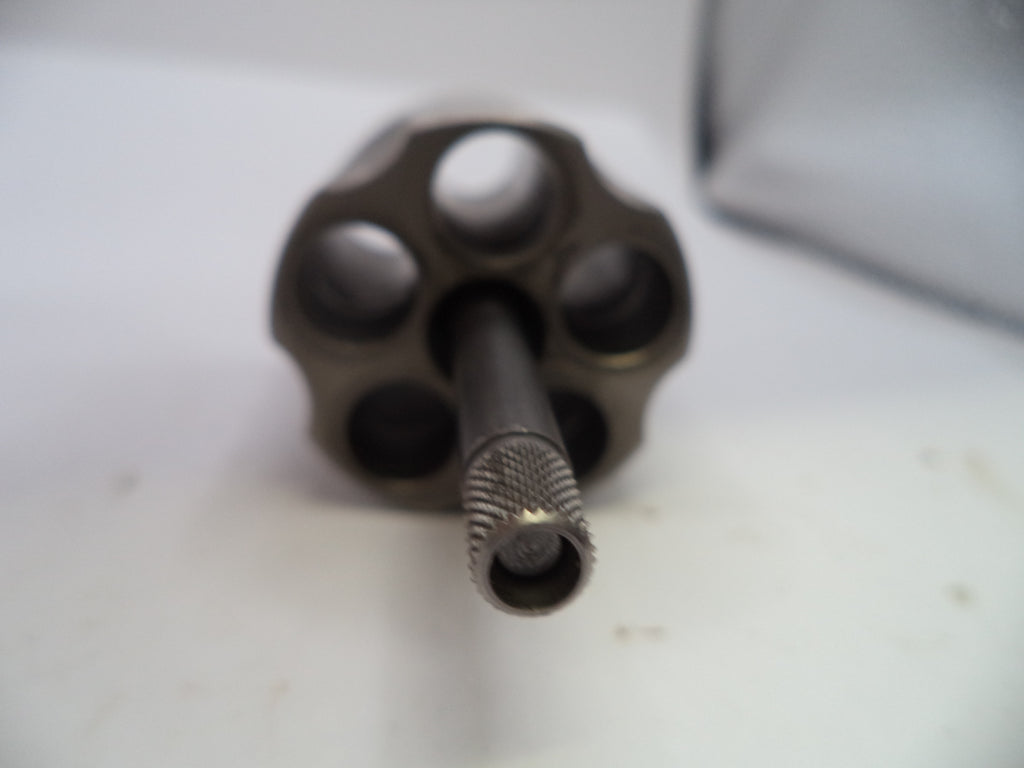 A close-up shot of a metallic revolver cylinder and barrel, showing a dark gunmetal finish on a white surface.