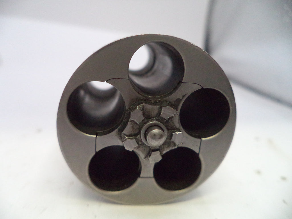 A close-up of a metallic circular component with four large dark openings and a central threaded or textured hub, photographed on a light gray to white background.