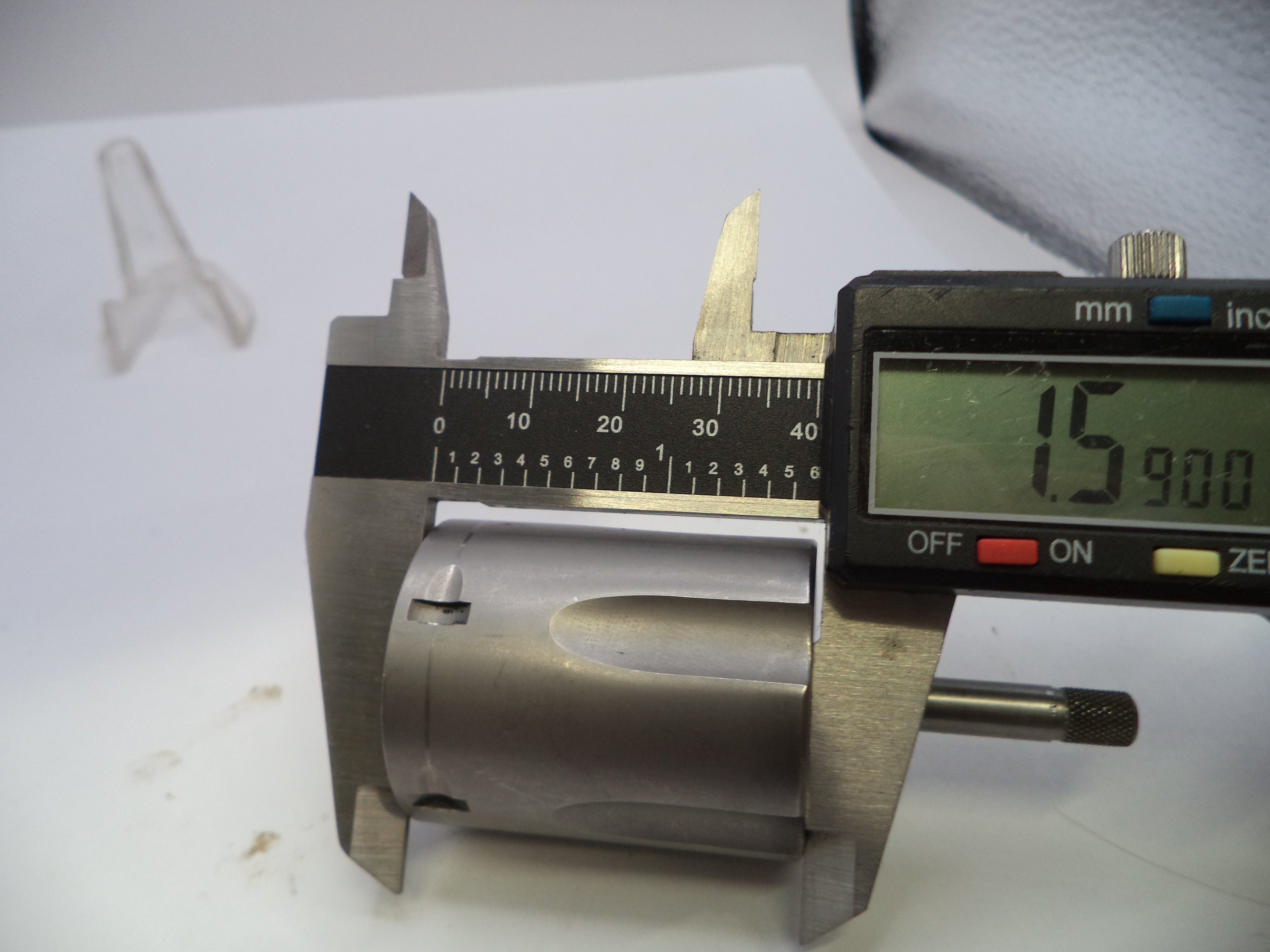 A metal caliper measuring a cylindrical metal component, with a digital display showing 15.900 mm.