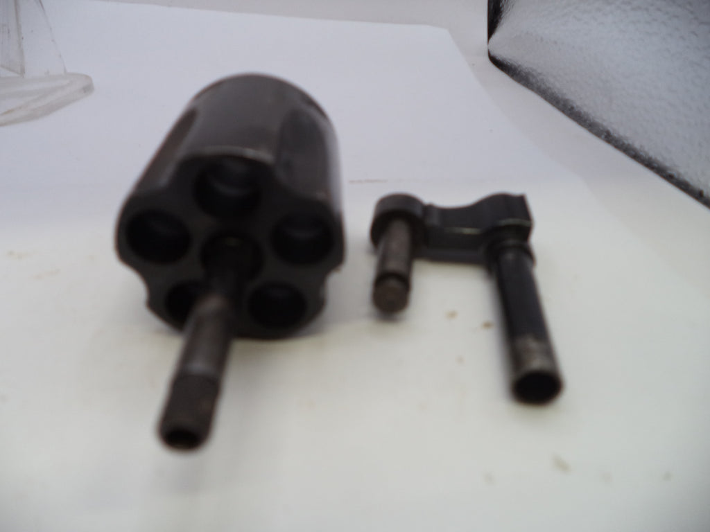 A black metal revolver cylinder and a black metal hand wheel tool, photographed on a white surface.