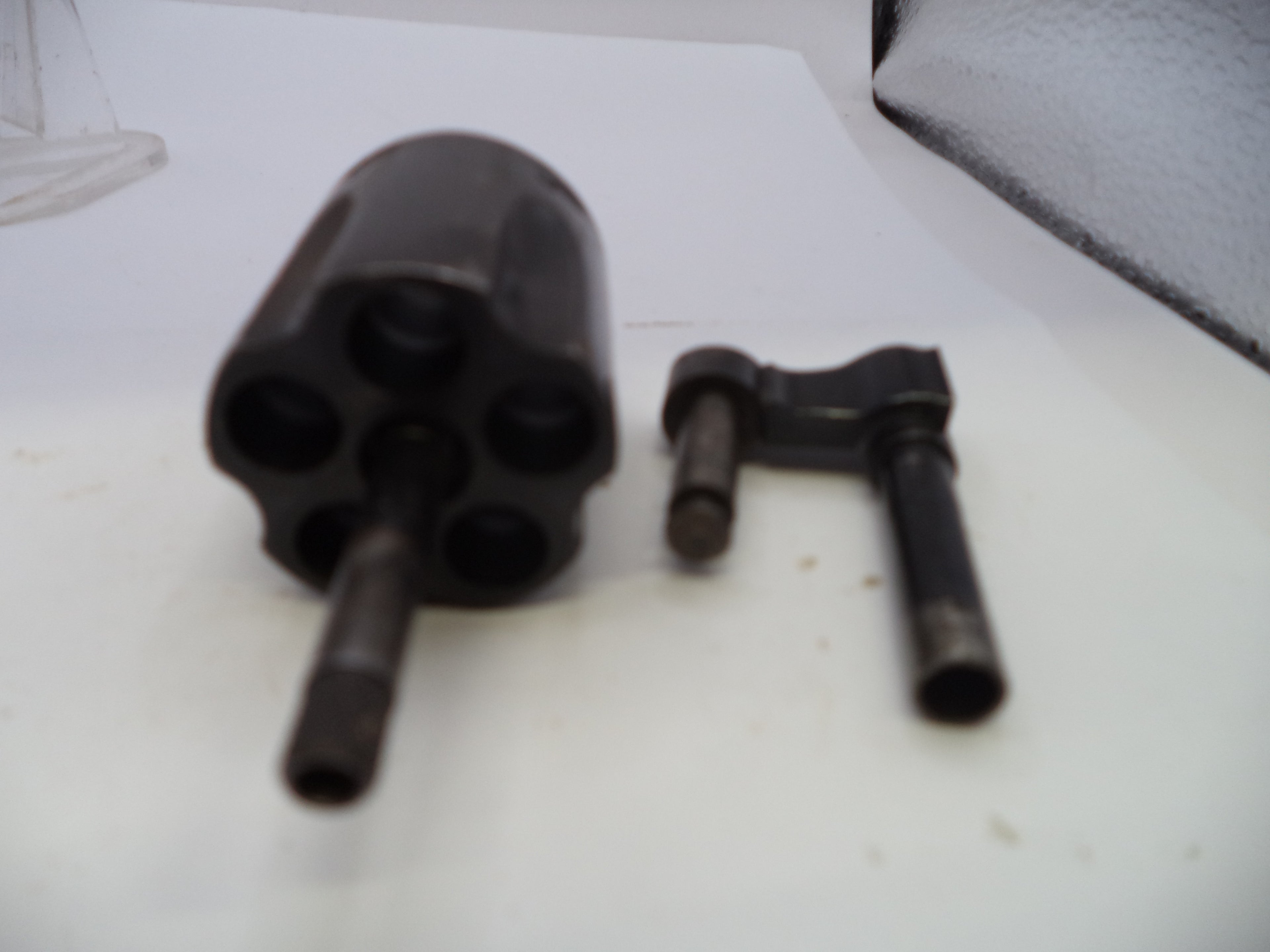 A black metal revolver cylinder and a black metal hand wheel tool, photographed on a white surface.