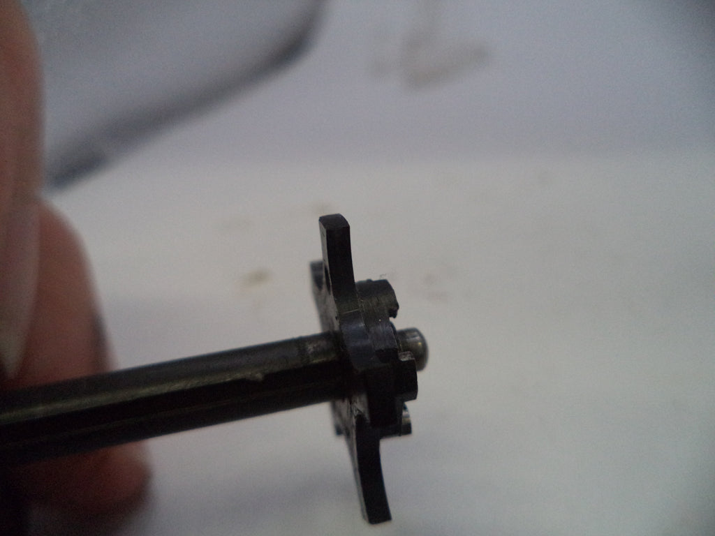 A close-up of a small black metal mechanical component held by fingers against a light, out-of-focus background.