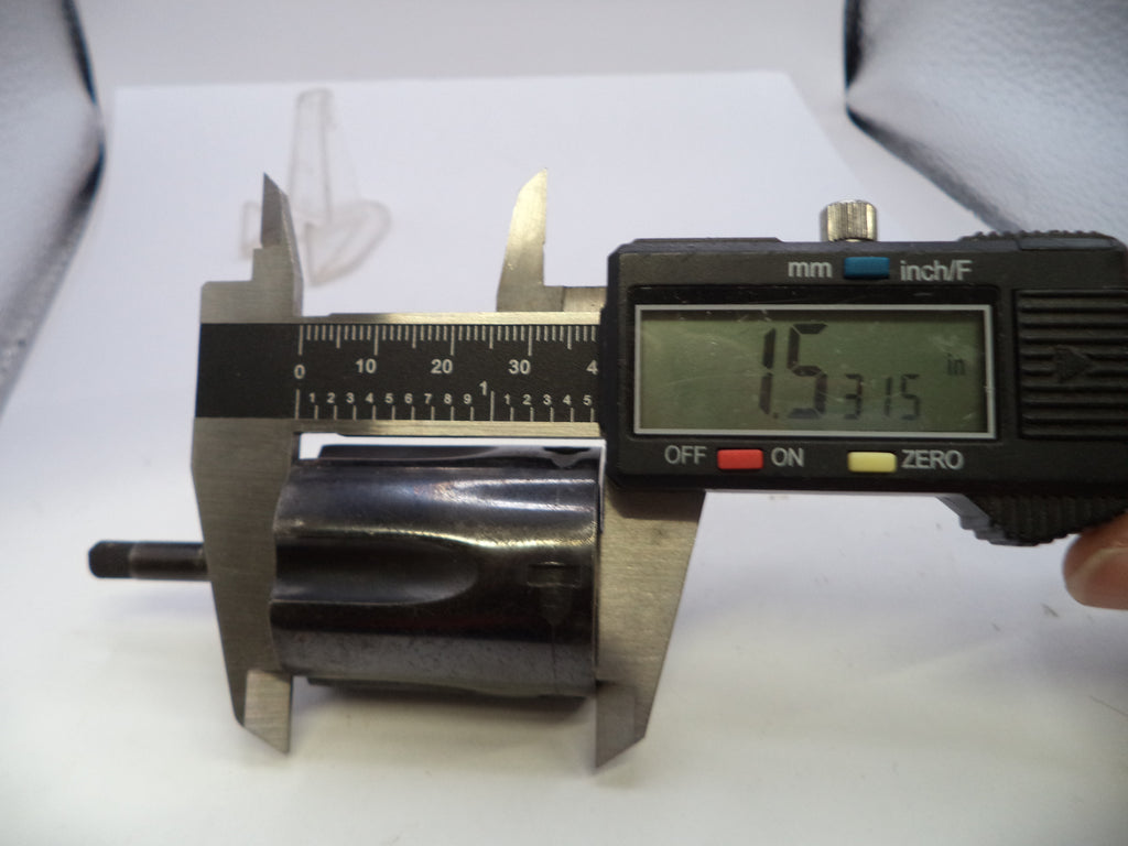 A digital caliper measuring a dark metallic cylindrical component on a white surface, with a hand holding the caliper's black display unit.