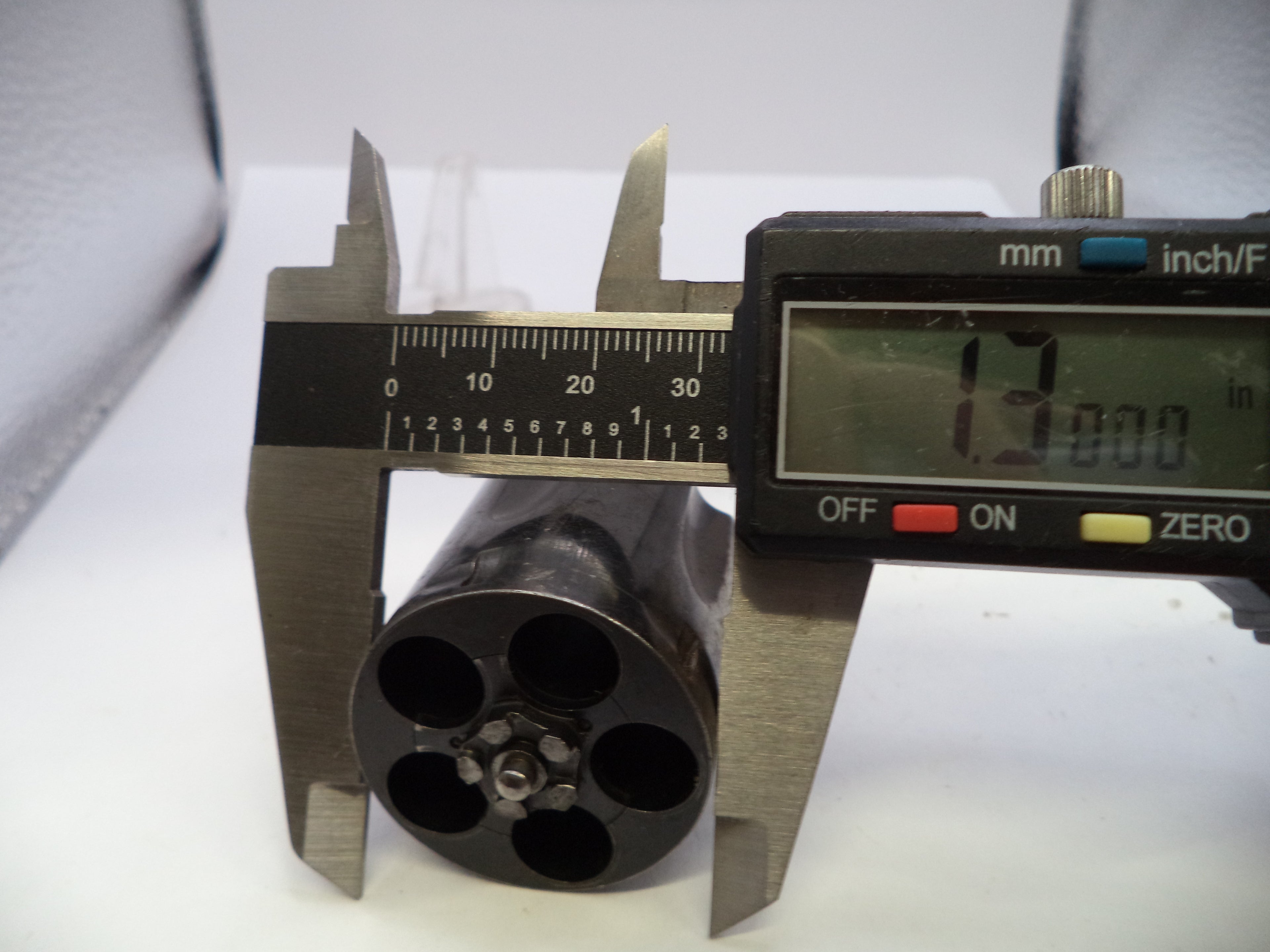 A close-up of a black cylindrical product with a six-hole pattern, measured by a digital caliper showing 12.000 mm.