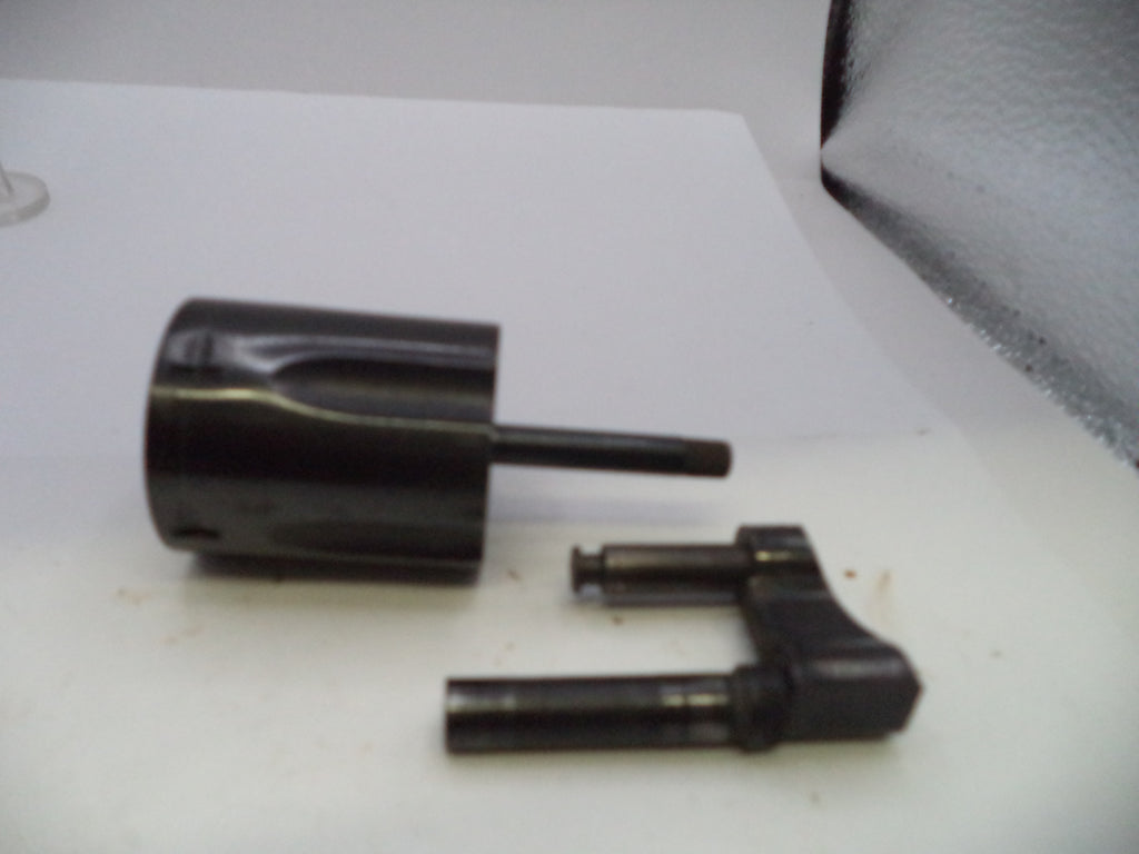 A black plastic or metal cylindrical component with a protruding rod, shown alongside a separate matching black mechanical piece on a white surface.