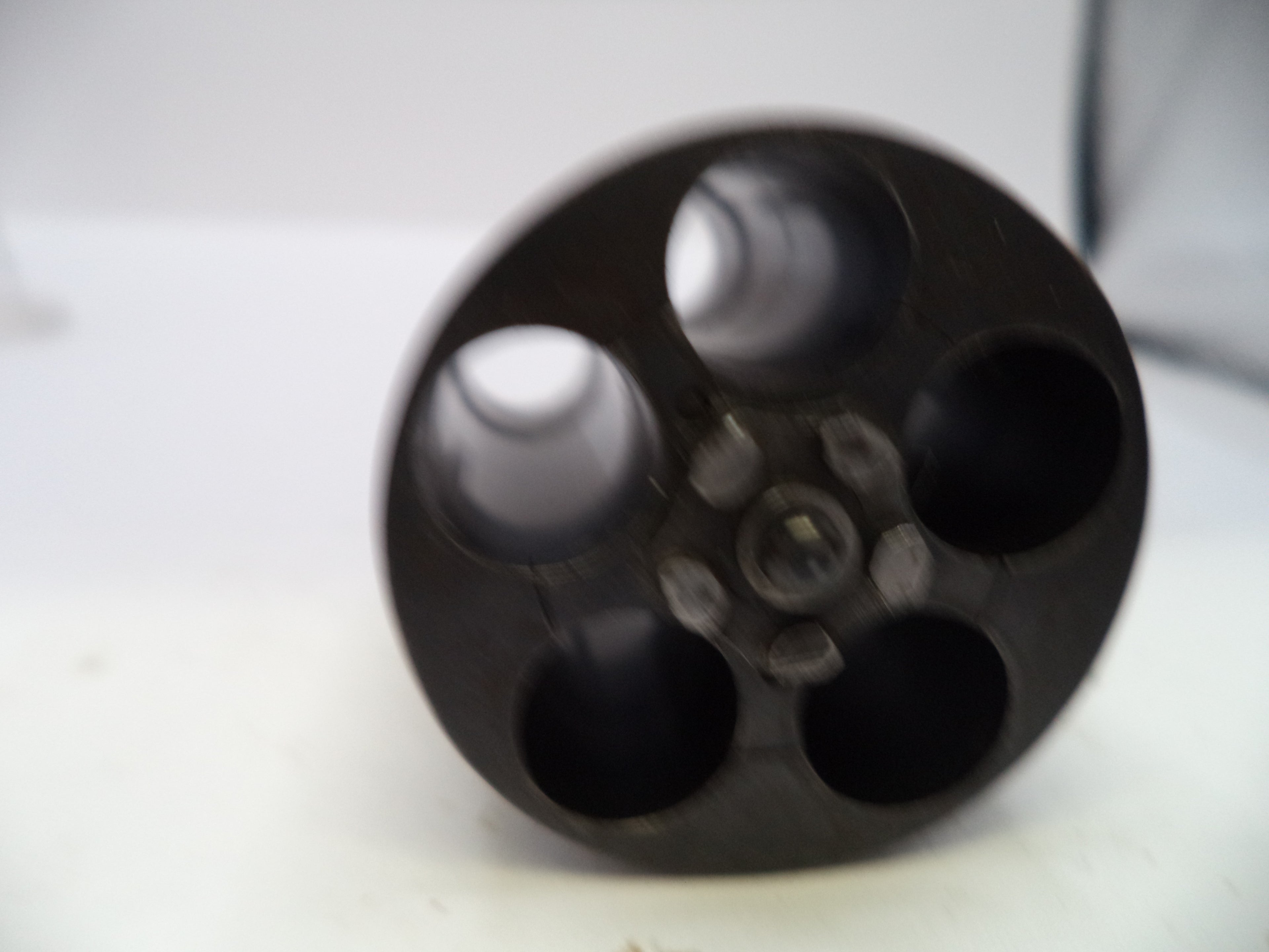A close-up of a black plastic multi-portable container or cup with five circular openings, photographed on a white surface.