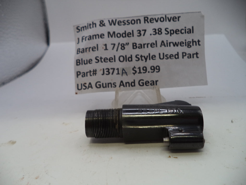 A black metal Smith & Wesson revolver barrel airweight part, shown on a white surface with a paper label card in the background.