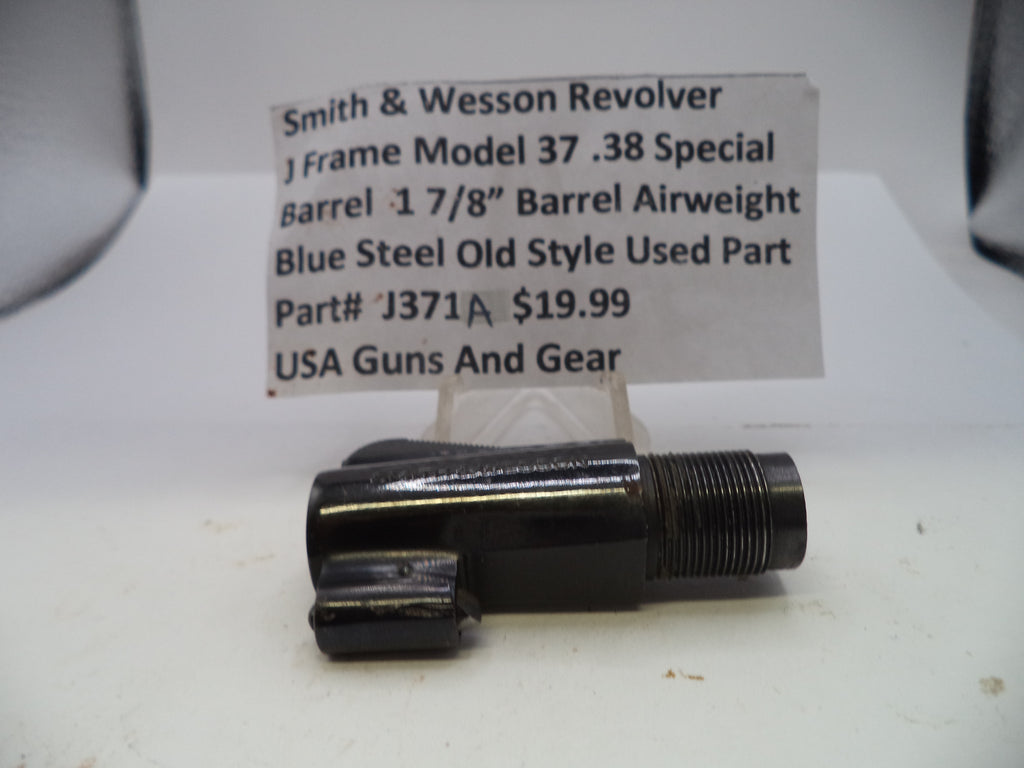 A used black metal Smith & Wesson revolver barrel part with a threaded end, displayed on a white surface with a handwritten price tag card behind it.