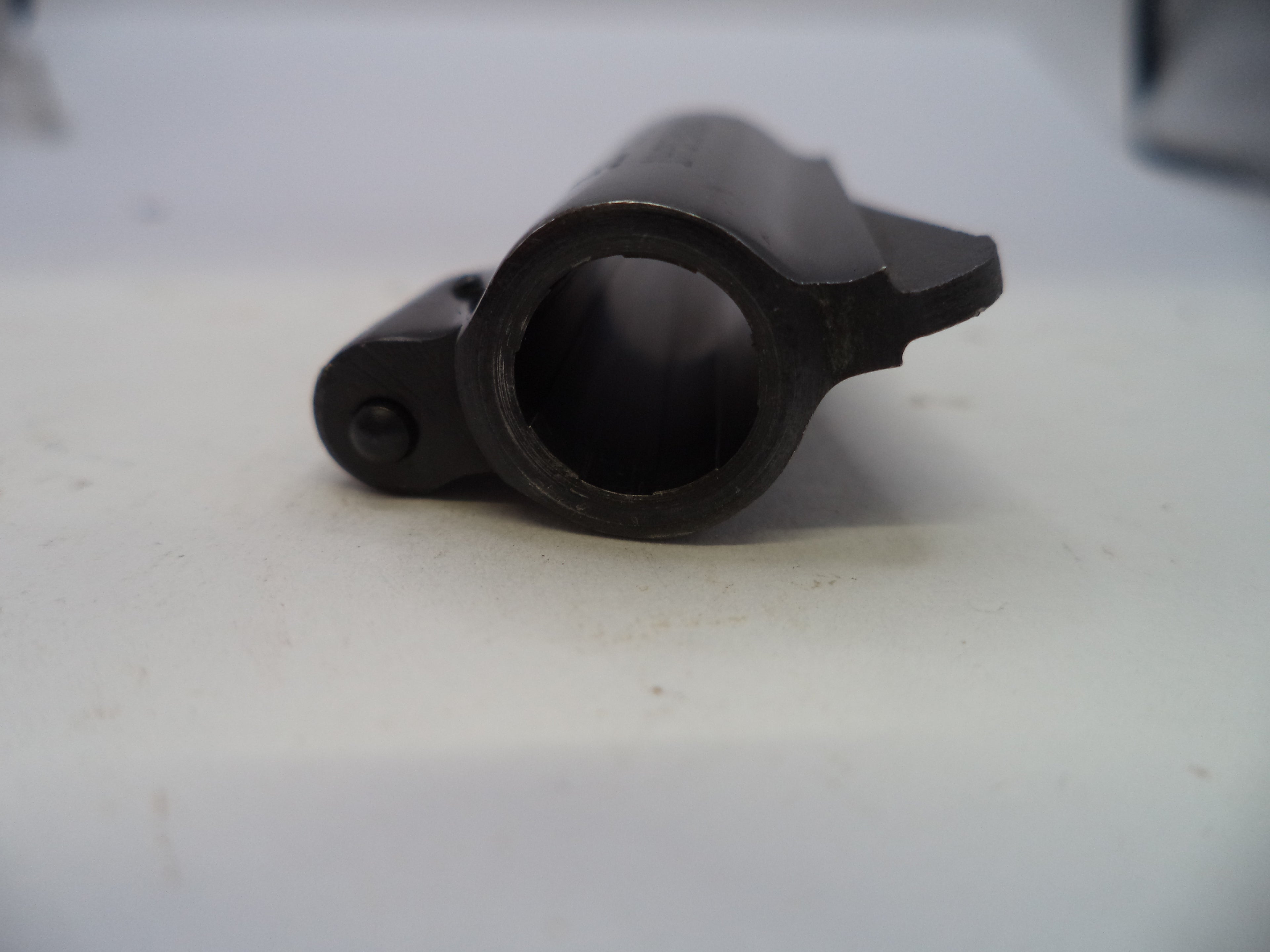 A close-up of a black metal cylindrical component with a circular opening and a small protruding tab, resting on a light-colored surface.