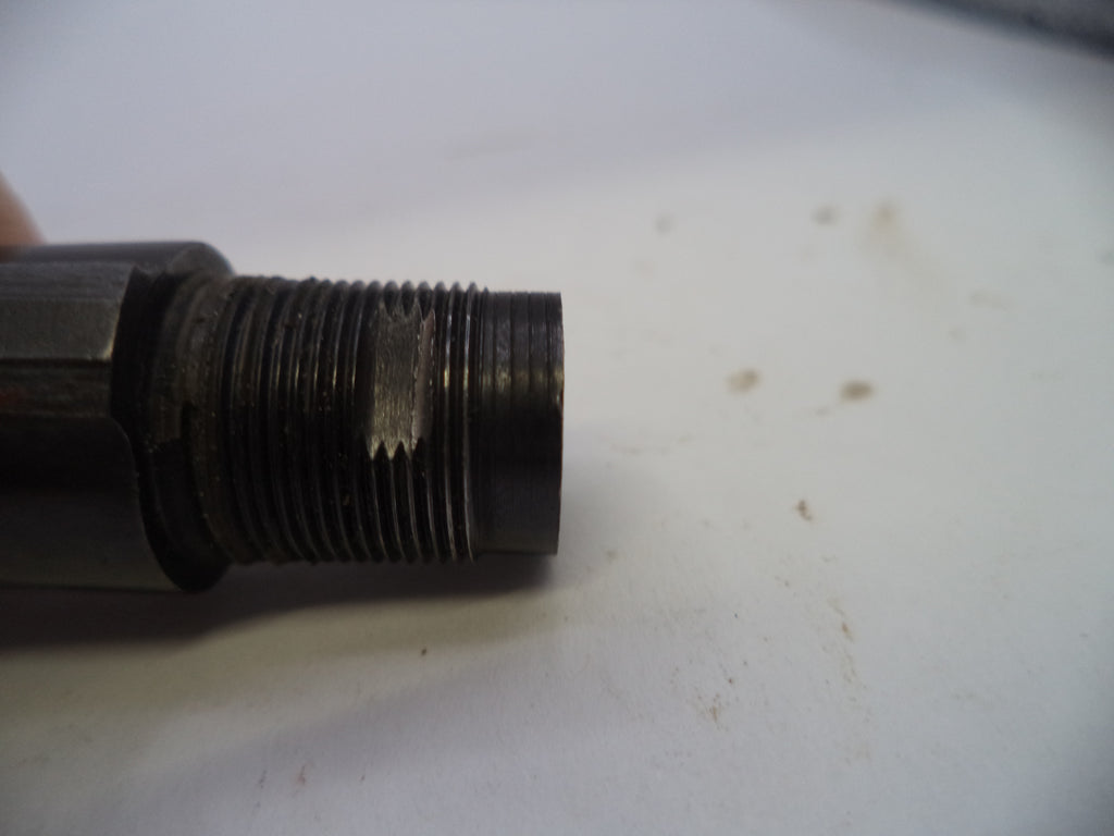 A close-up of a dark metal threaded component, possibly a mechanical fitting or valve stem, resting on a white surface.