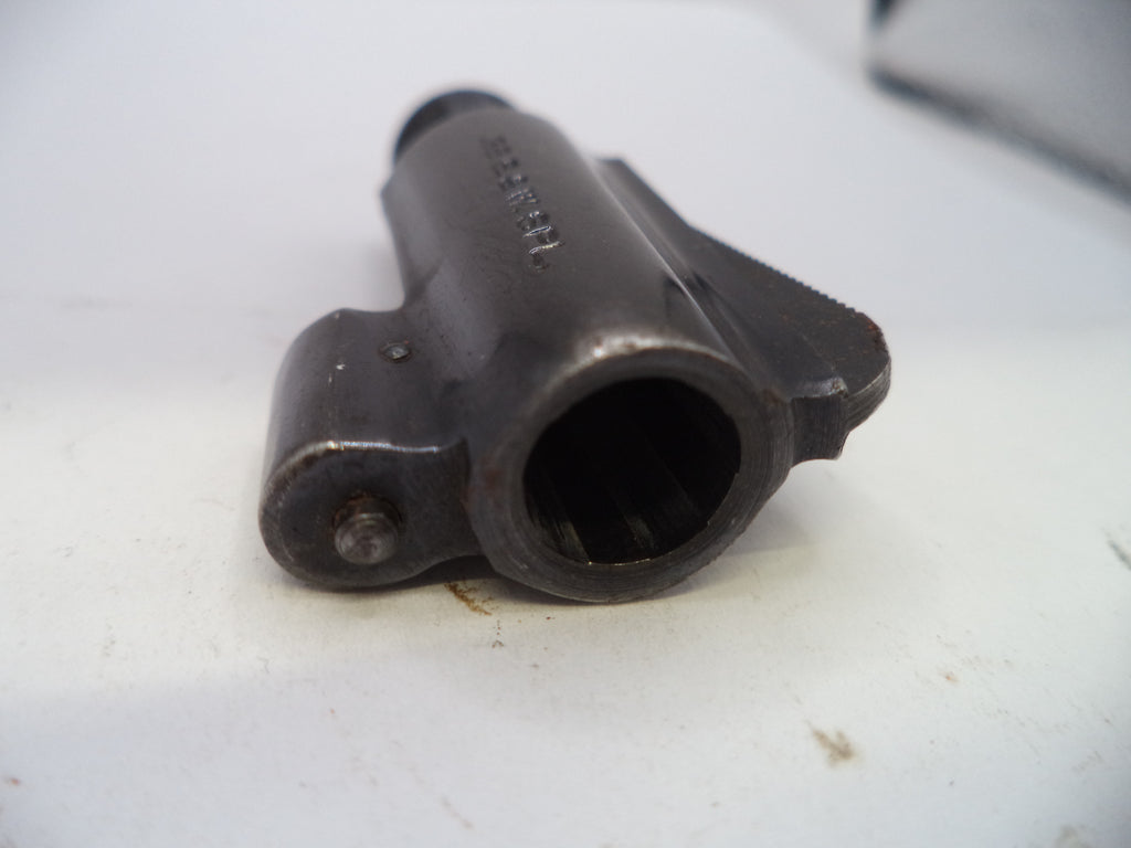 A close-up shot of a dark metal firearm component, specifically a receiver or barrel assembly with a visible bolt hole, resting on a white surface.