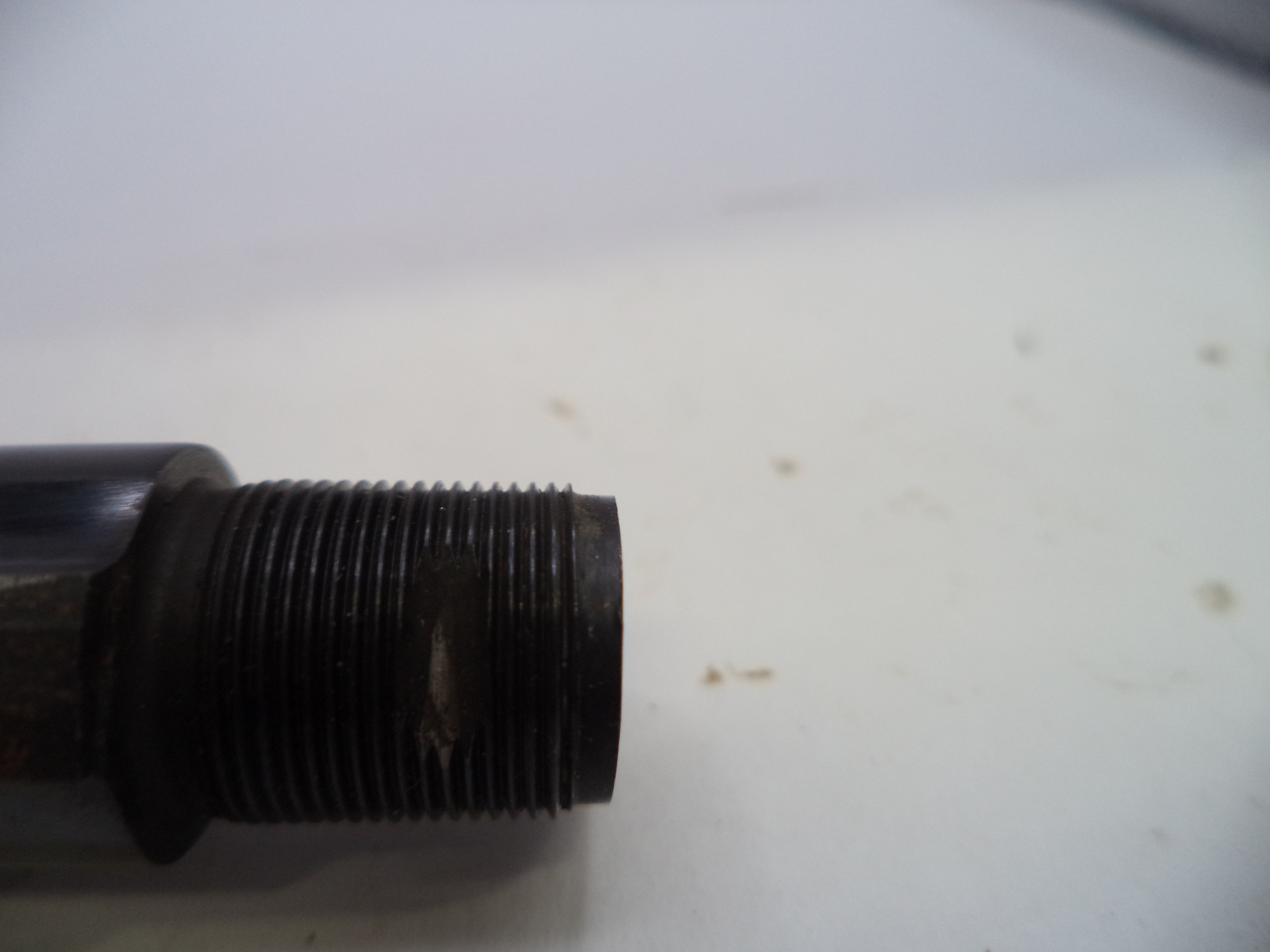 A close-up of a dark metal threaded pipe fitting or valve component on a white surface.