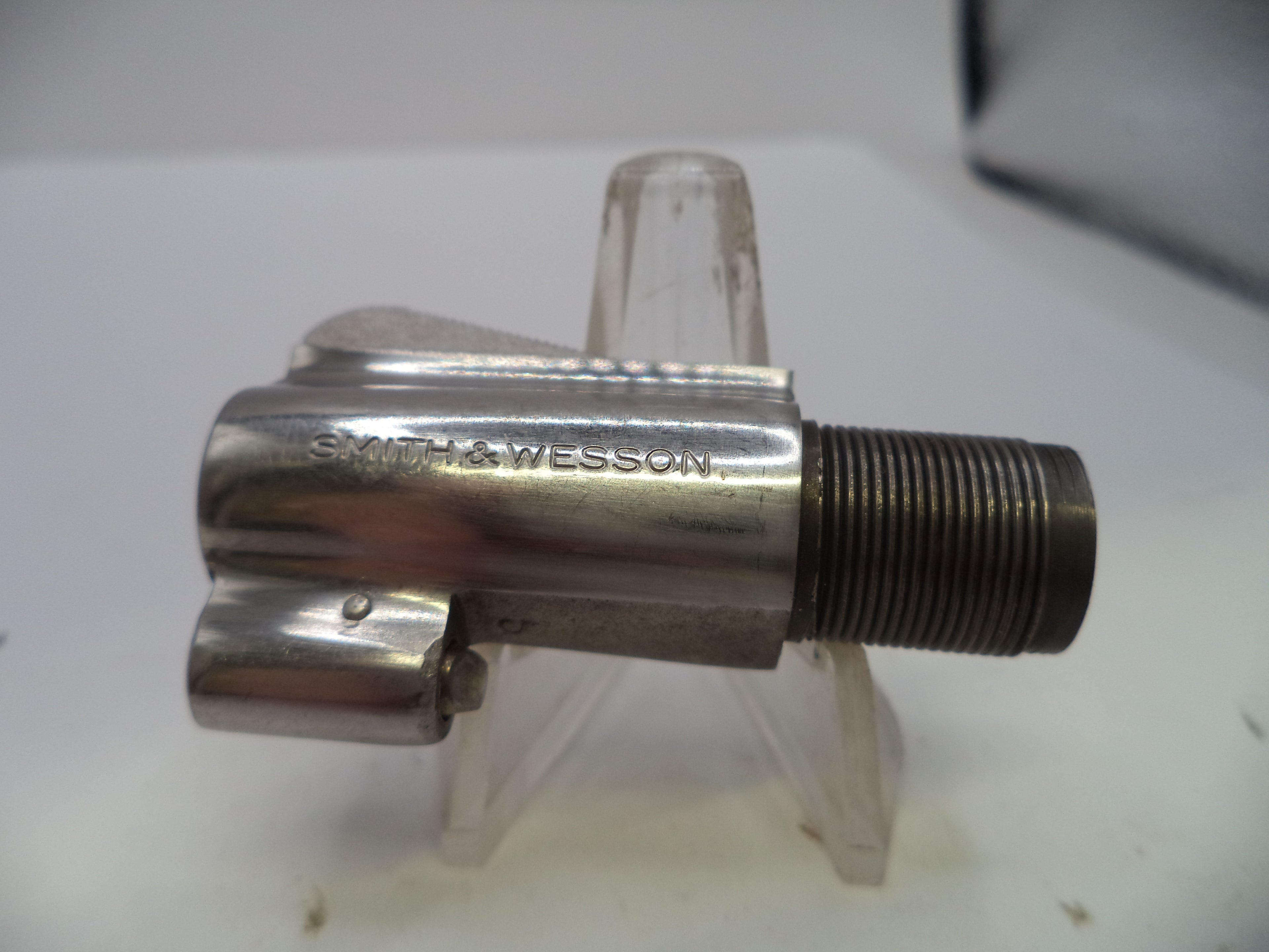 A metallic bicycle headset component with a threaded bearing race, featuring the engraved brand name 'SMITH & WESSON' on its polished shroud, displayed on a clear plastic stand.