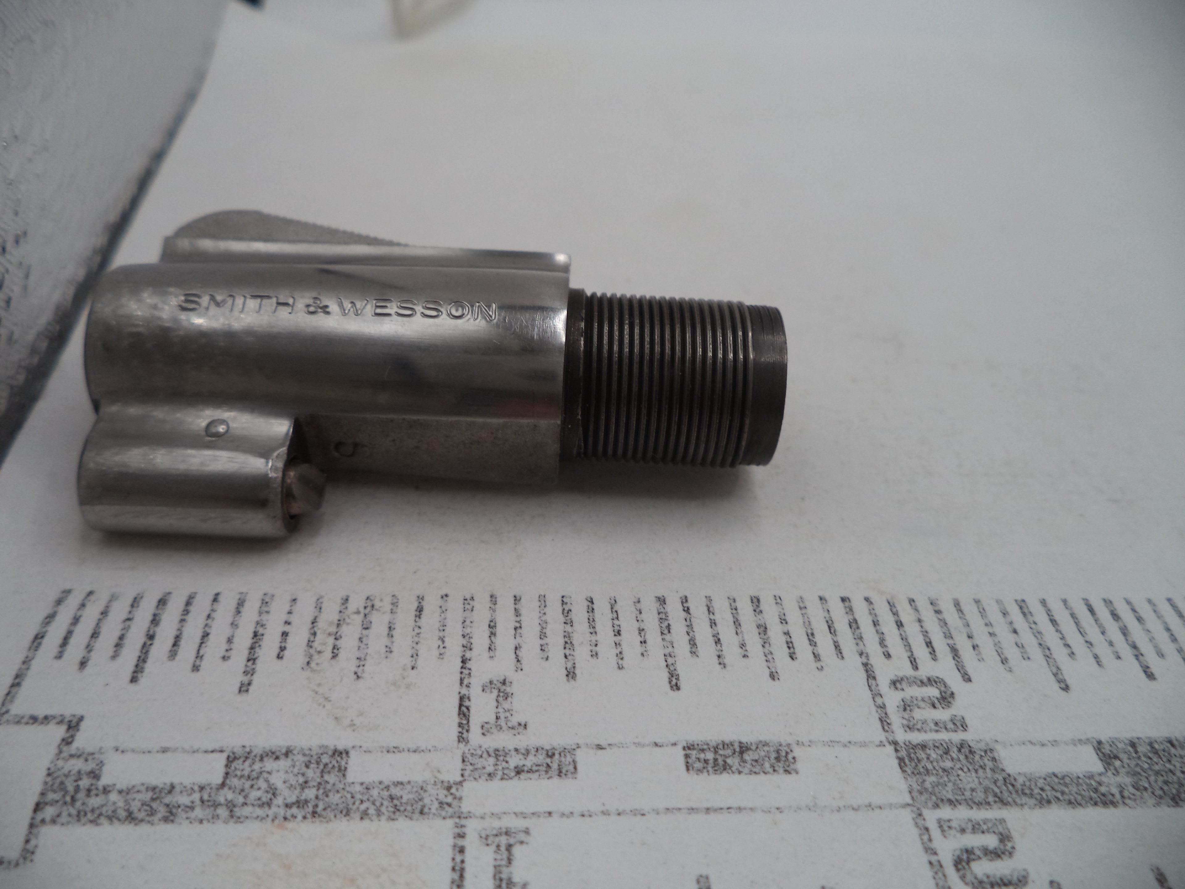 A vintage metal Smith & Wesson tool or hardware component with a threaded male end, resting on a printed paper background.