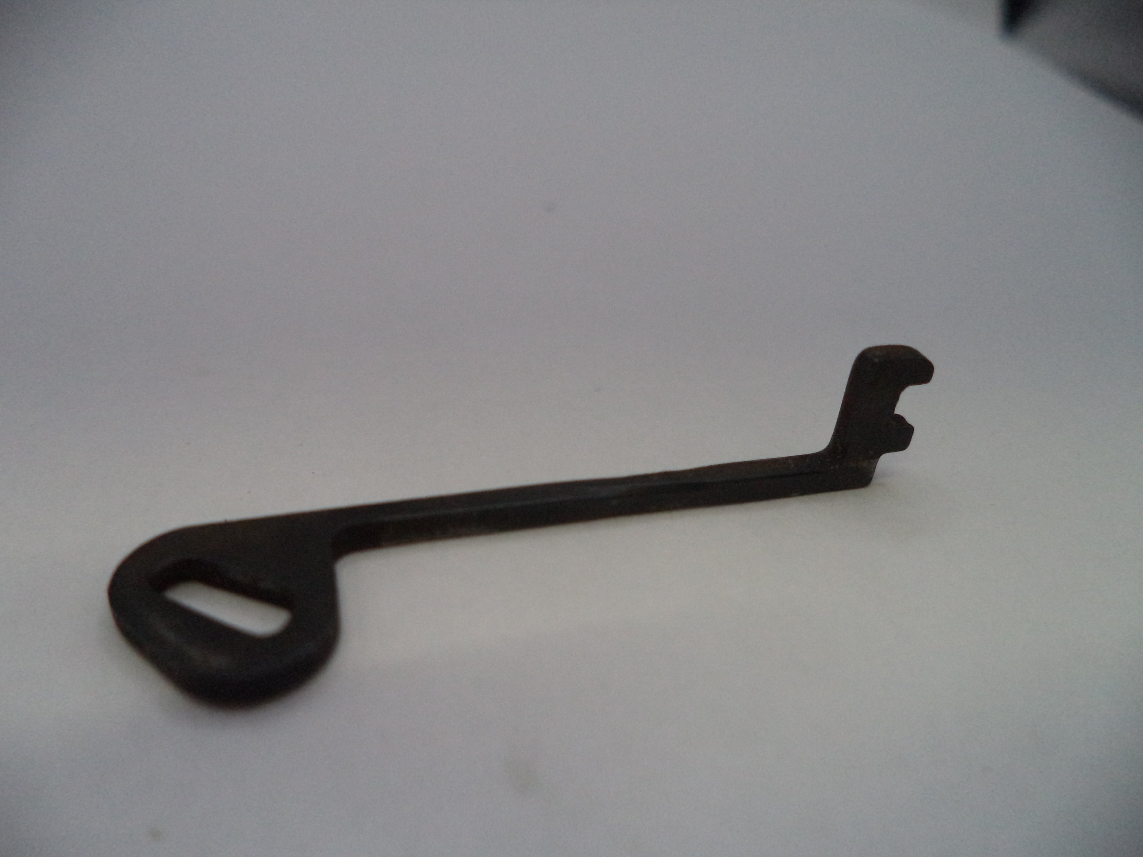 A small dark metal key-shaped tool with a looped handle and bent tip, photographed on a plain light background.