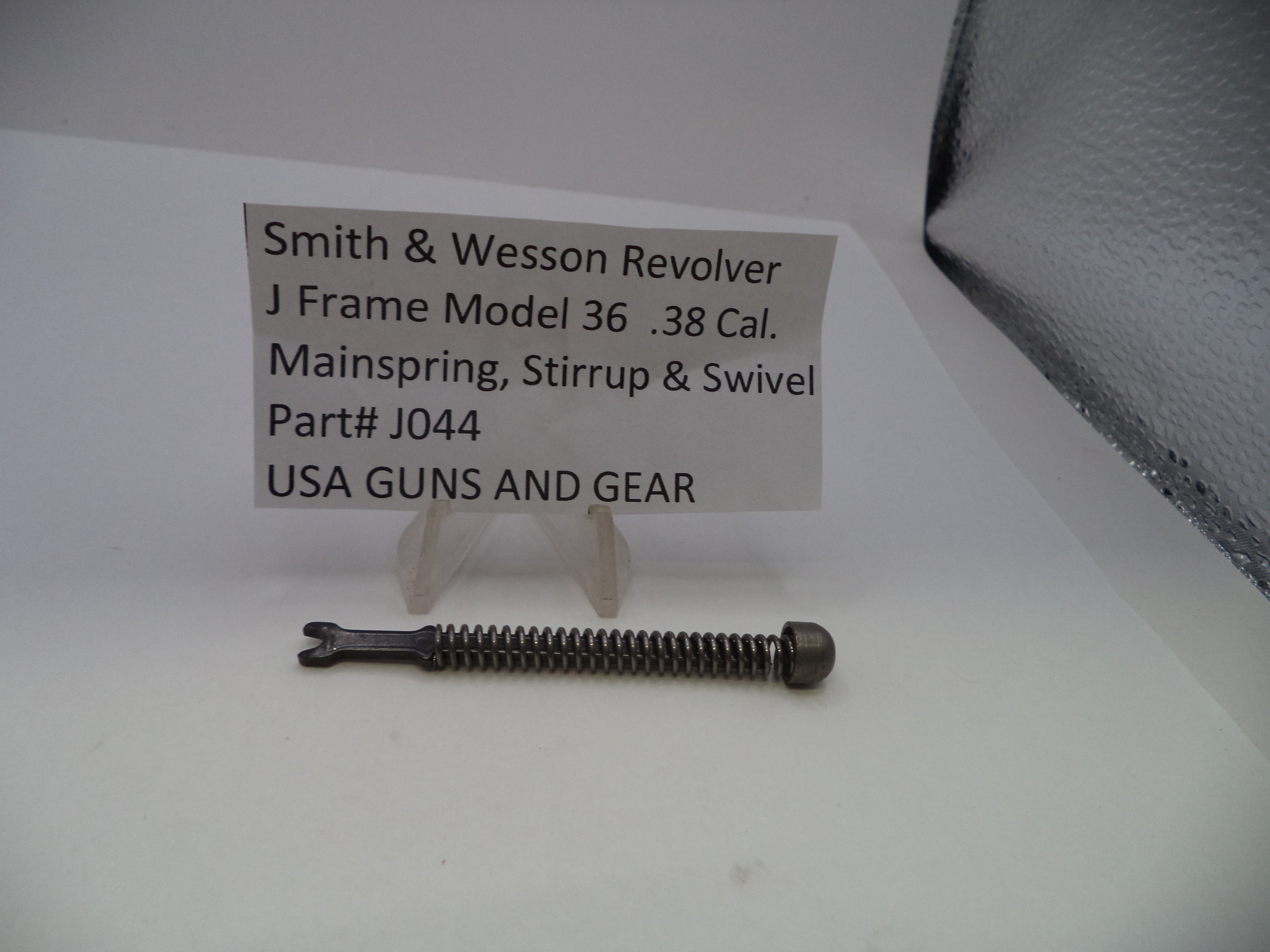A single metal screw part displayed on a white surface with a small sign reading 'Smith & Wesson Revolver J Frame Model 36 .38 Cal.
