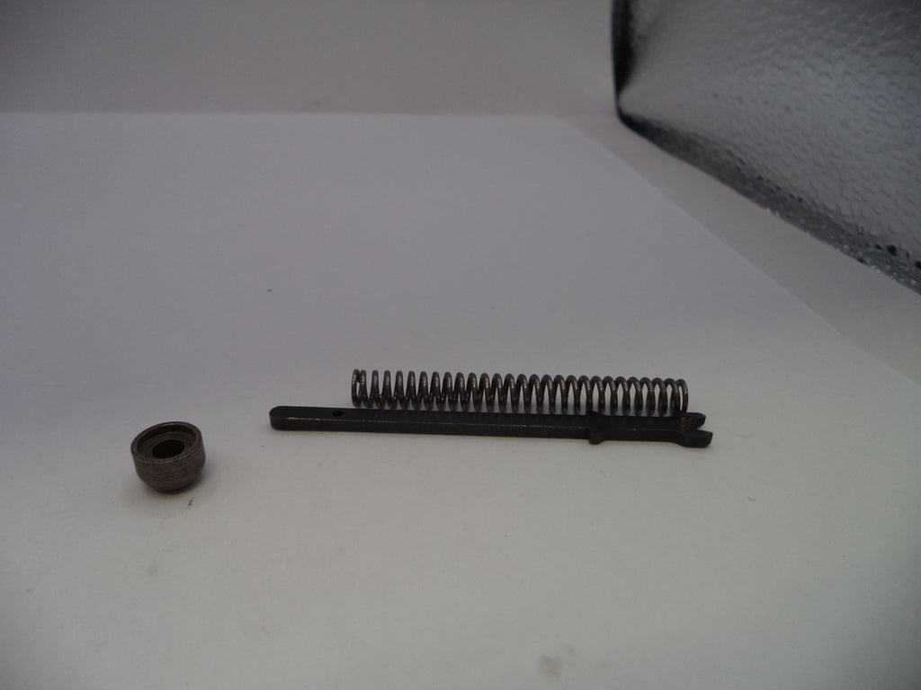 A small metal mechanical component set on a white surface, featuring a dark metal spring and a separate small circular piece.