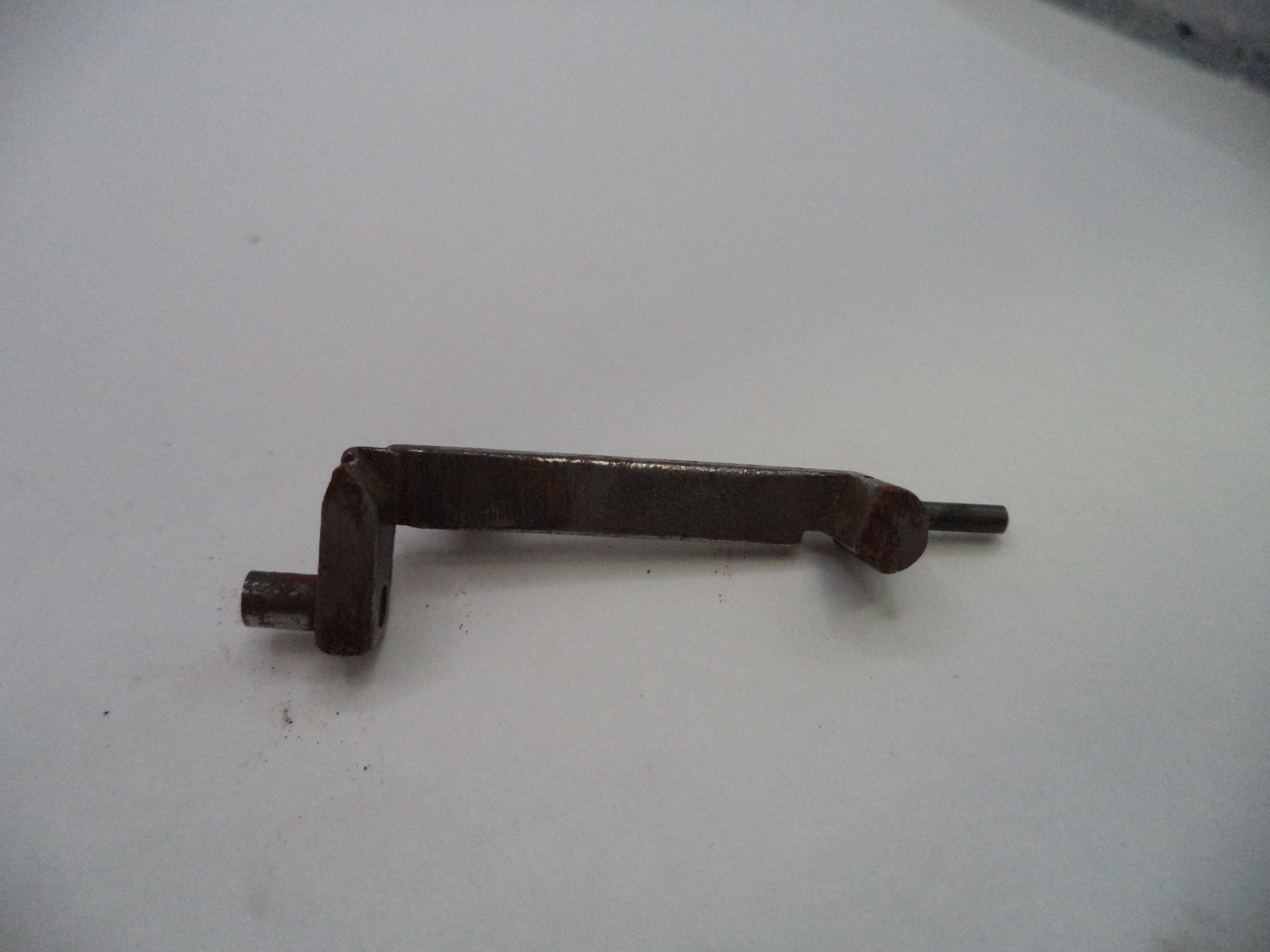 A small dark metal mechanical part with a bent shaft and cylindrical end, photographed on a plain light background.