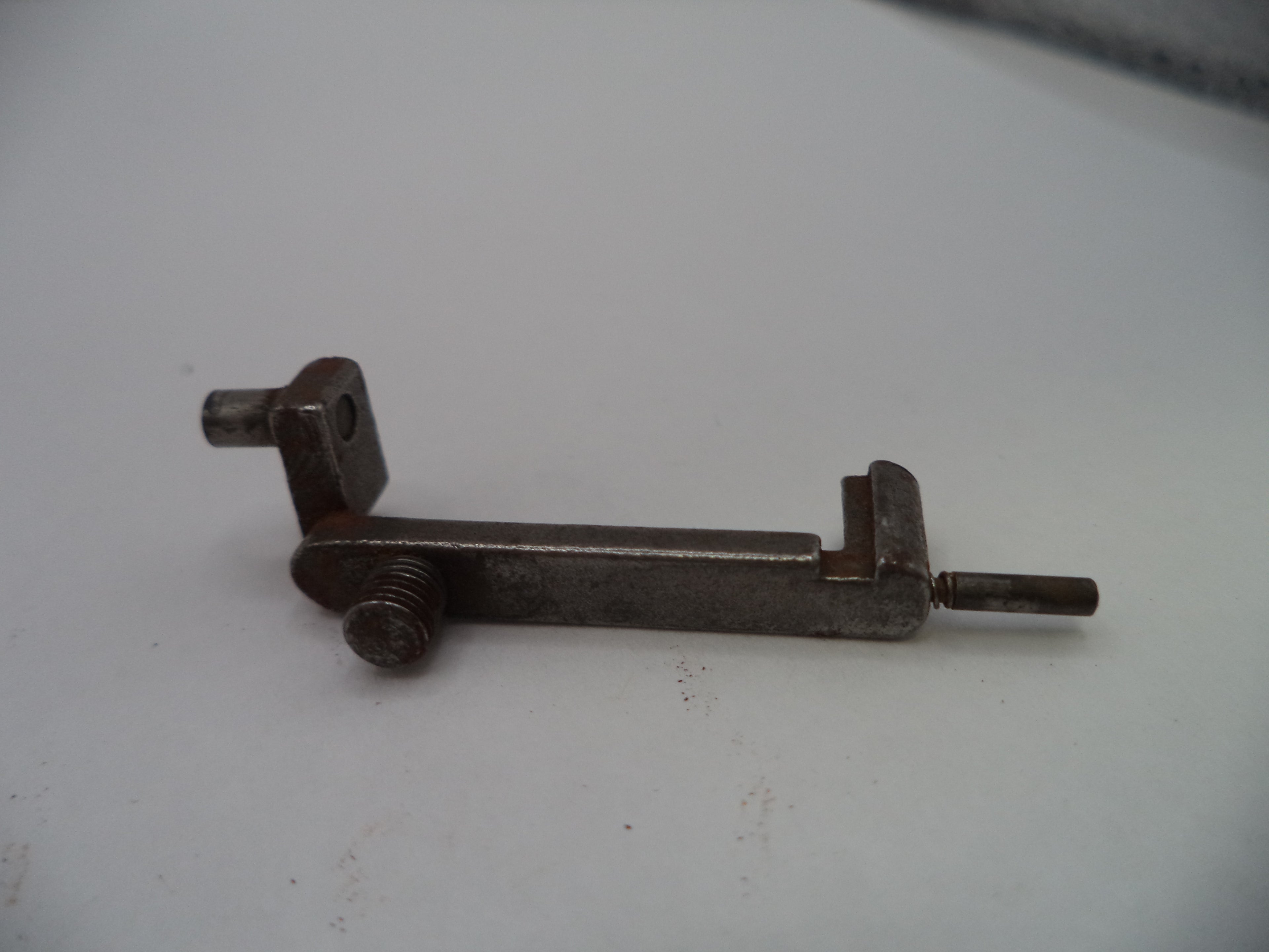 A small metal mechanical component or latch with a threaded screw and a flat shaft, photographed on a plain light background.