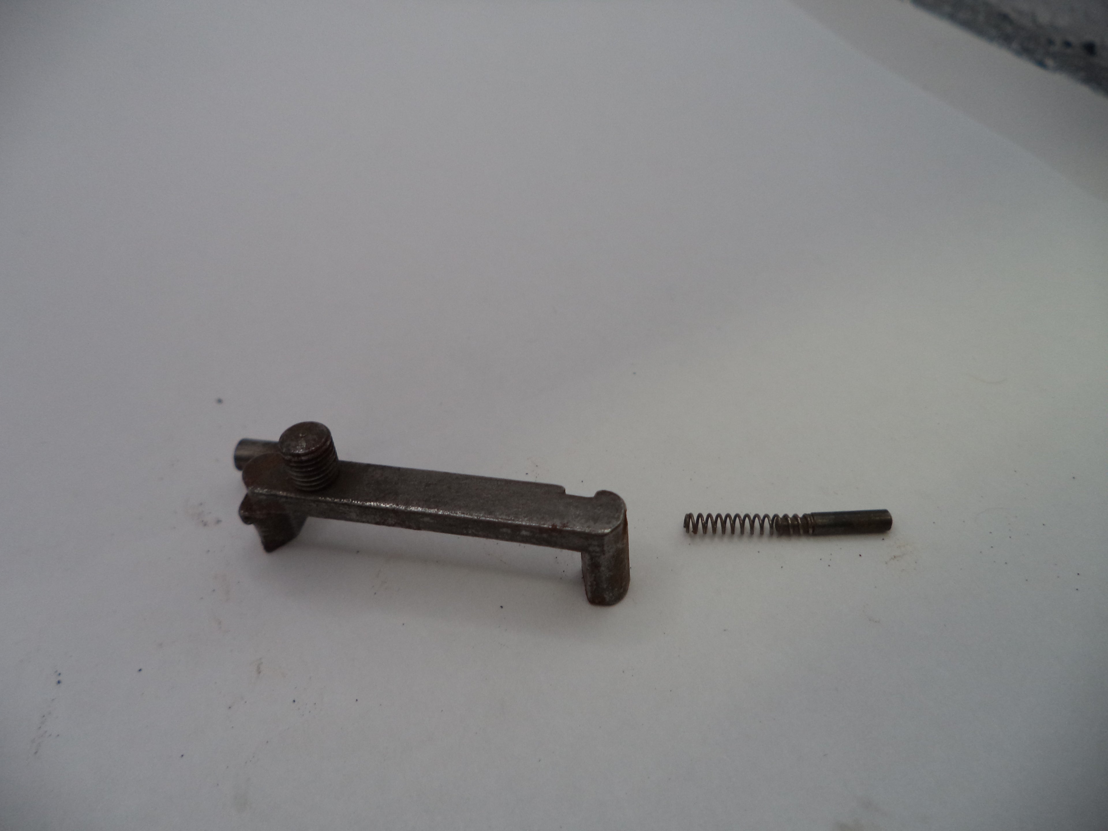 A small metal mechanical component with a spring and pin, shown on a plain light gray surface.