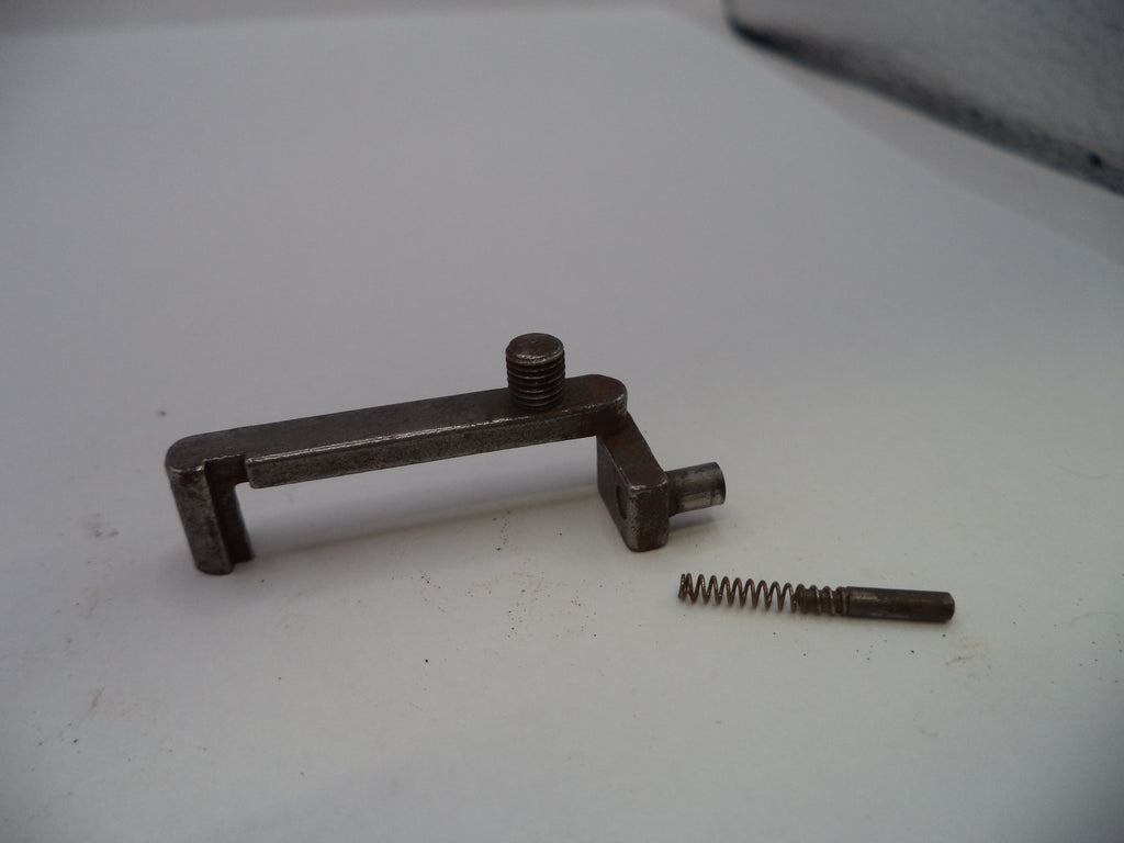 A small metal mechanical component with a screw and a separate coiled spring, photographed on a plain light surface.