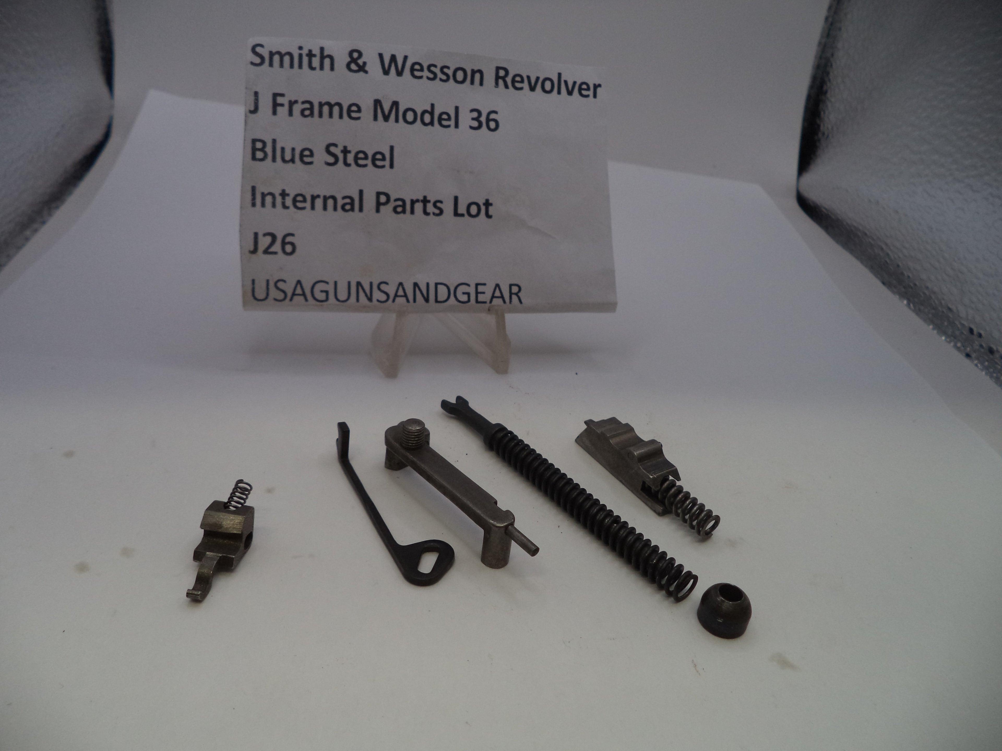 Internal parts lot for a Smith & Wesson Revolver J Frame Model 36 in blue steel, containing various metal components and springs, displayed on a white surface with a paper label in the background.