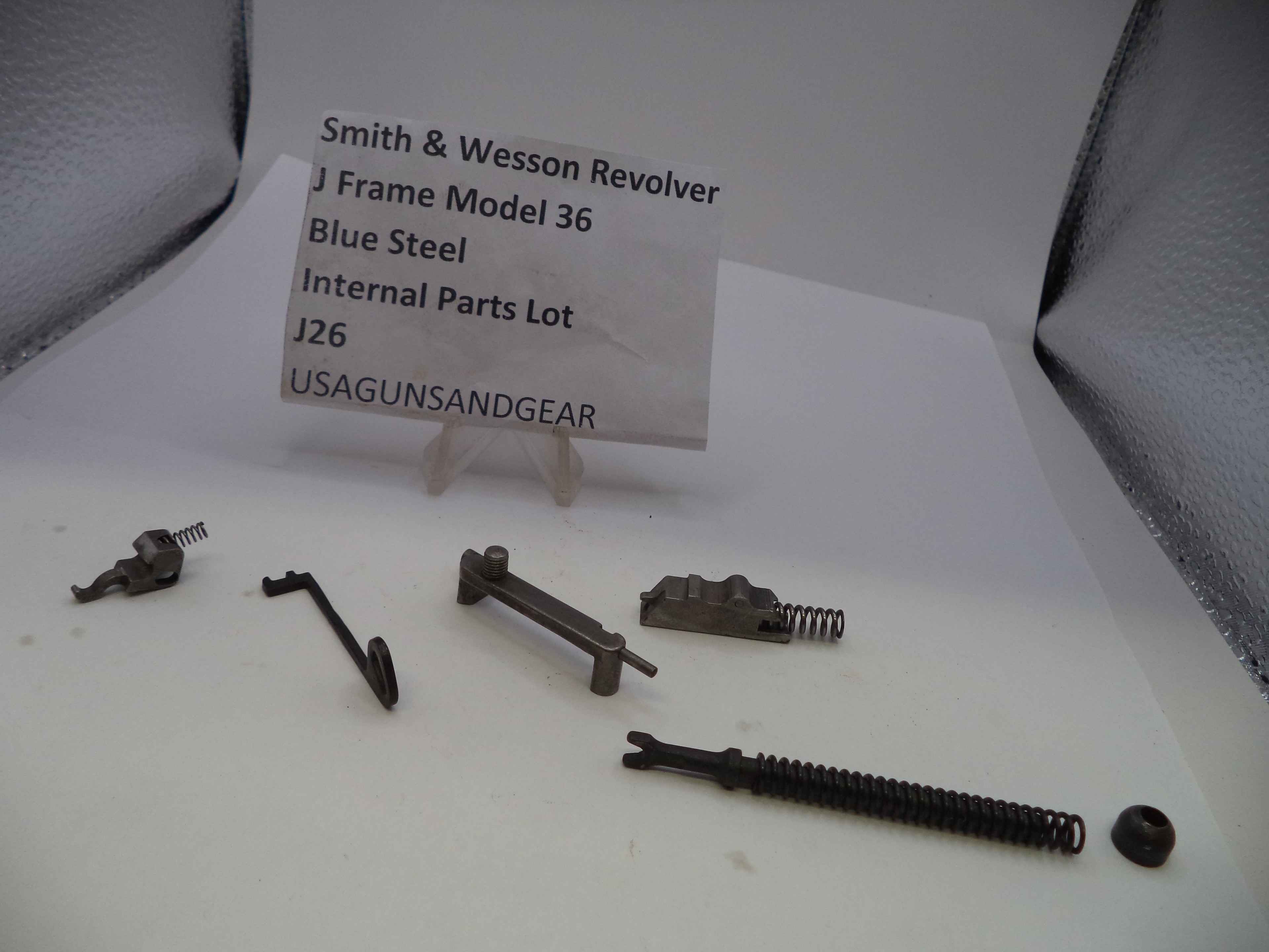 Internal parts lot of Smith & Wesson Revolver J Frame Model 36 blue steel components, including springs, pins, and a latch, displayed on a white surface with a paper label card.