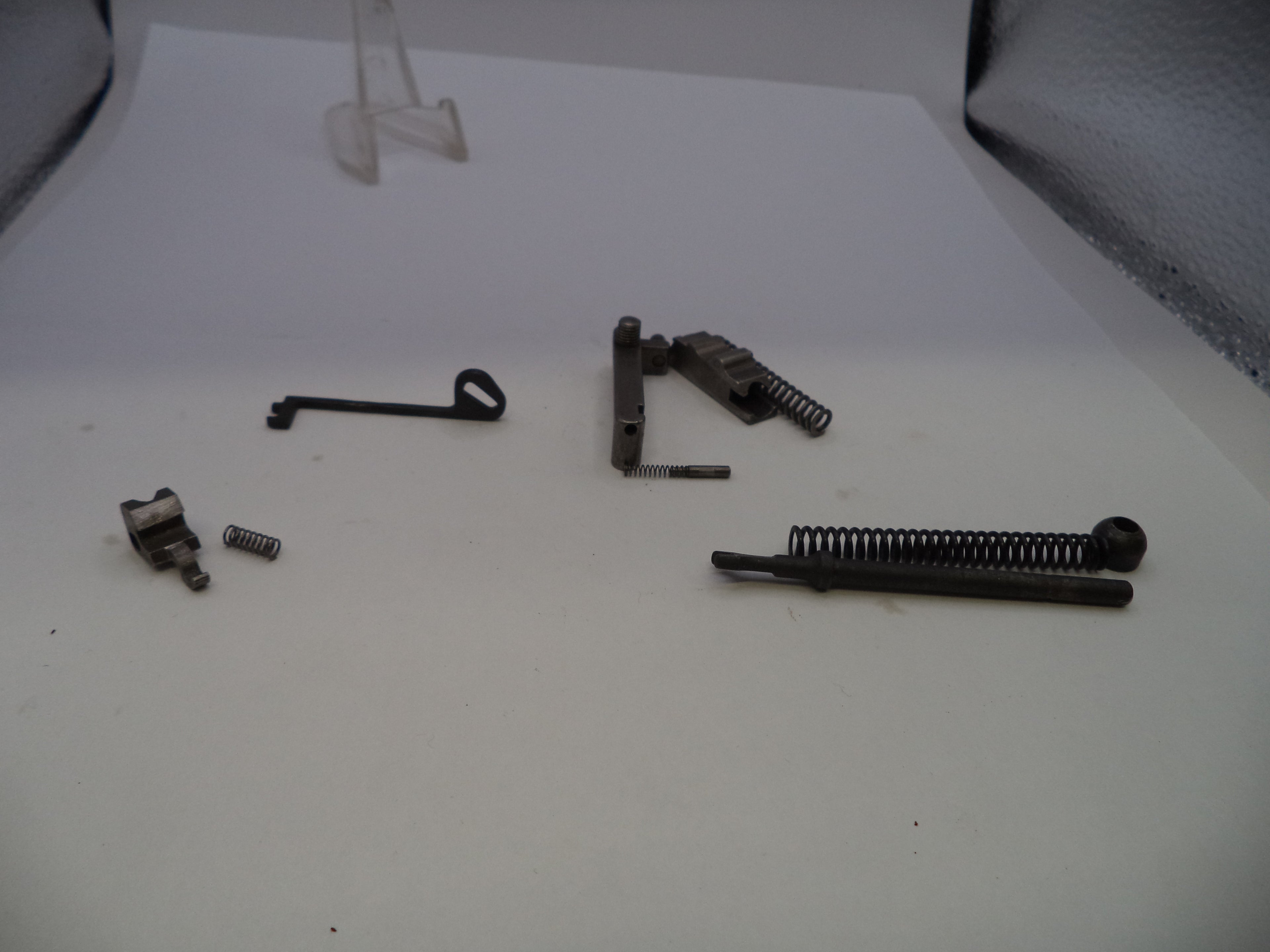 A set of disassembled metal firearm components, including springs, rods, and small metal parts, arranged on a white surface.