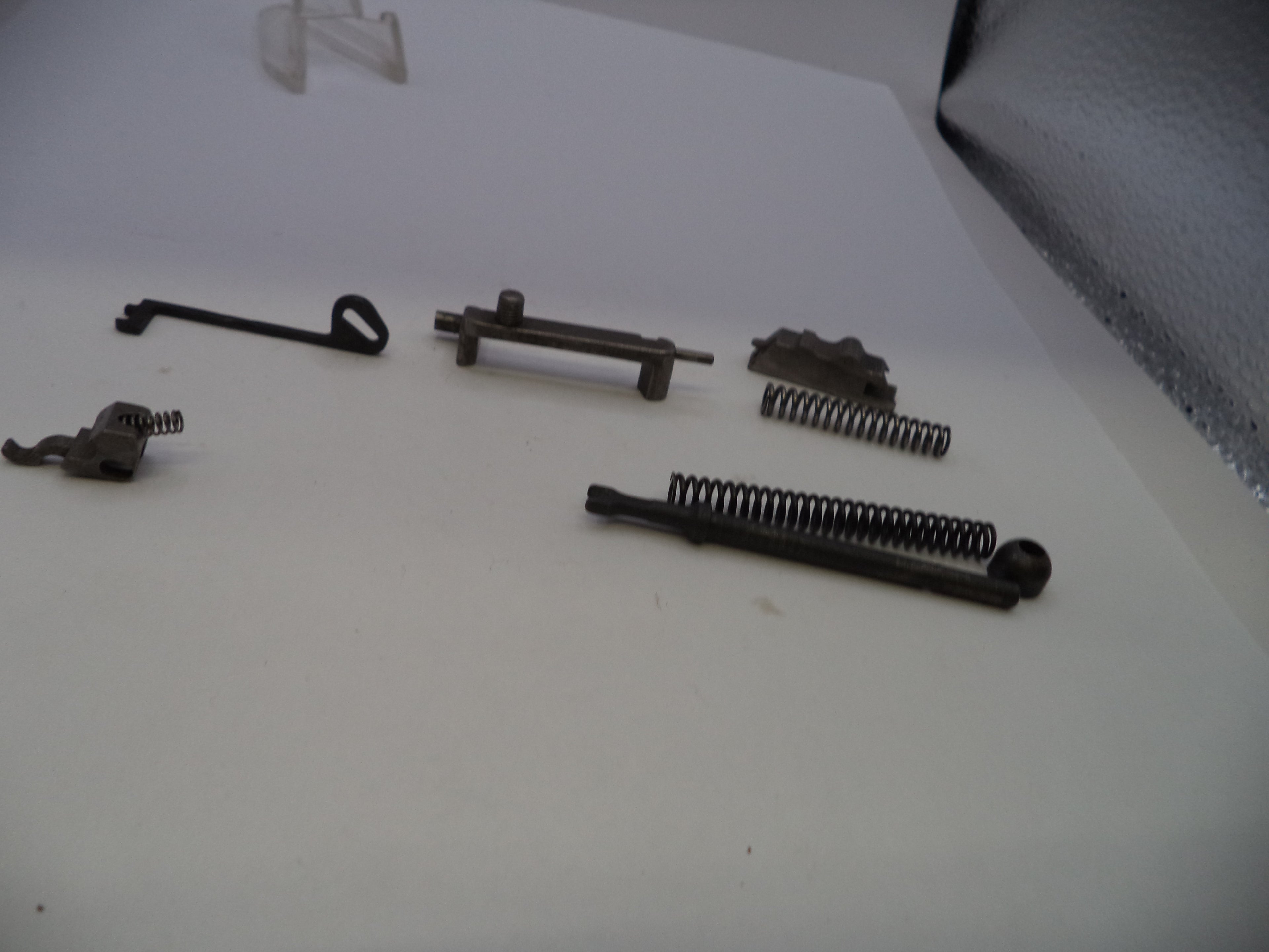 A set of small metal mechanical parts and springs arranged on a plain white surface.