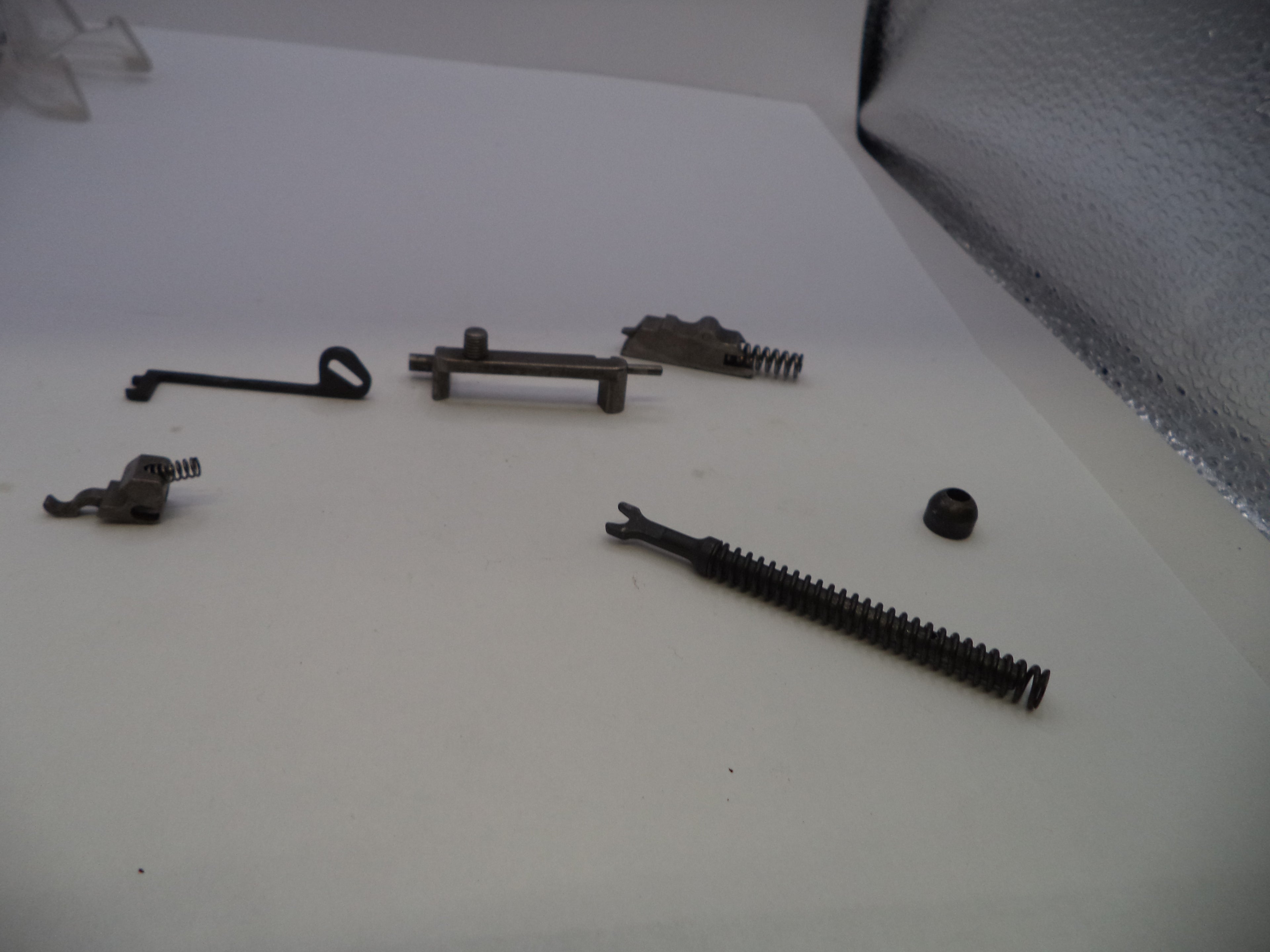 A set of small dark metal mechanical parts and springs arranged on a plain white surface.