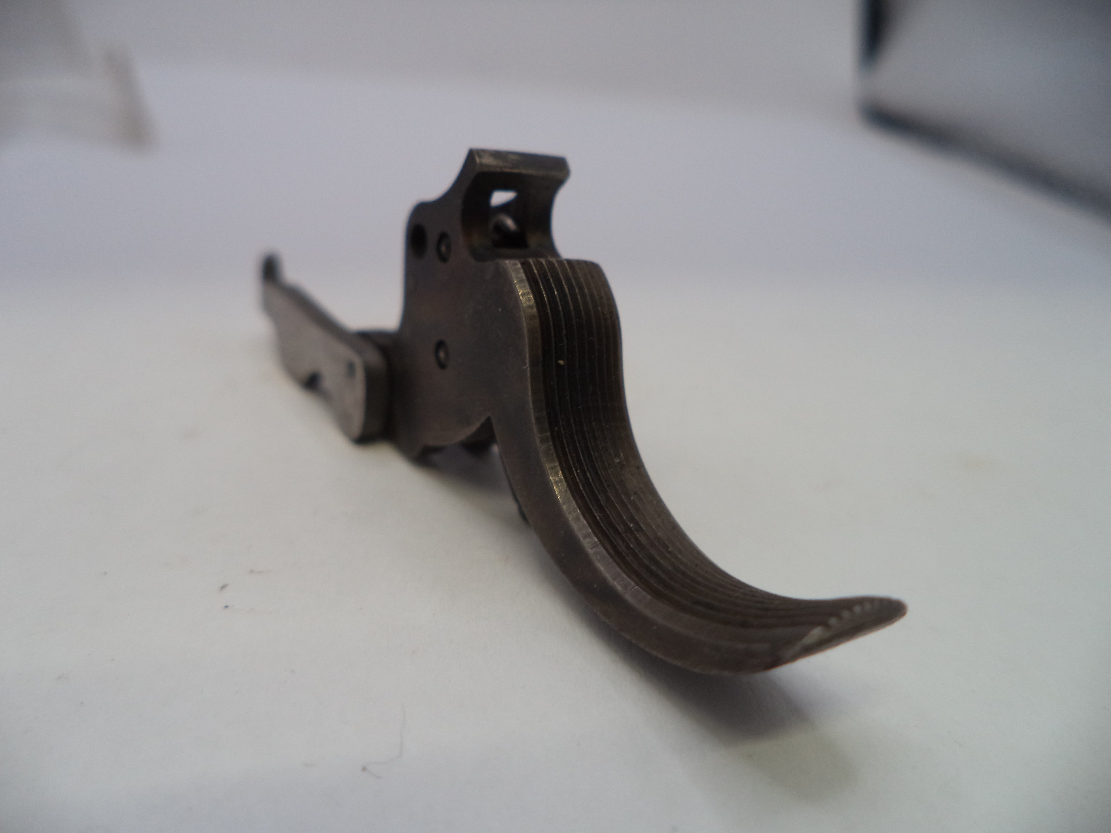 A close-up of a dark metal trigger assembly or lever component on a plain light background.