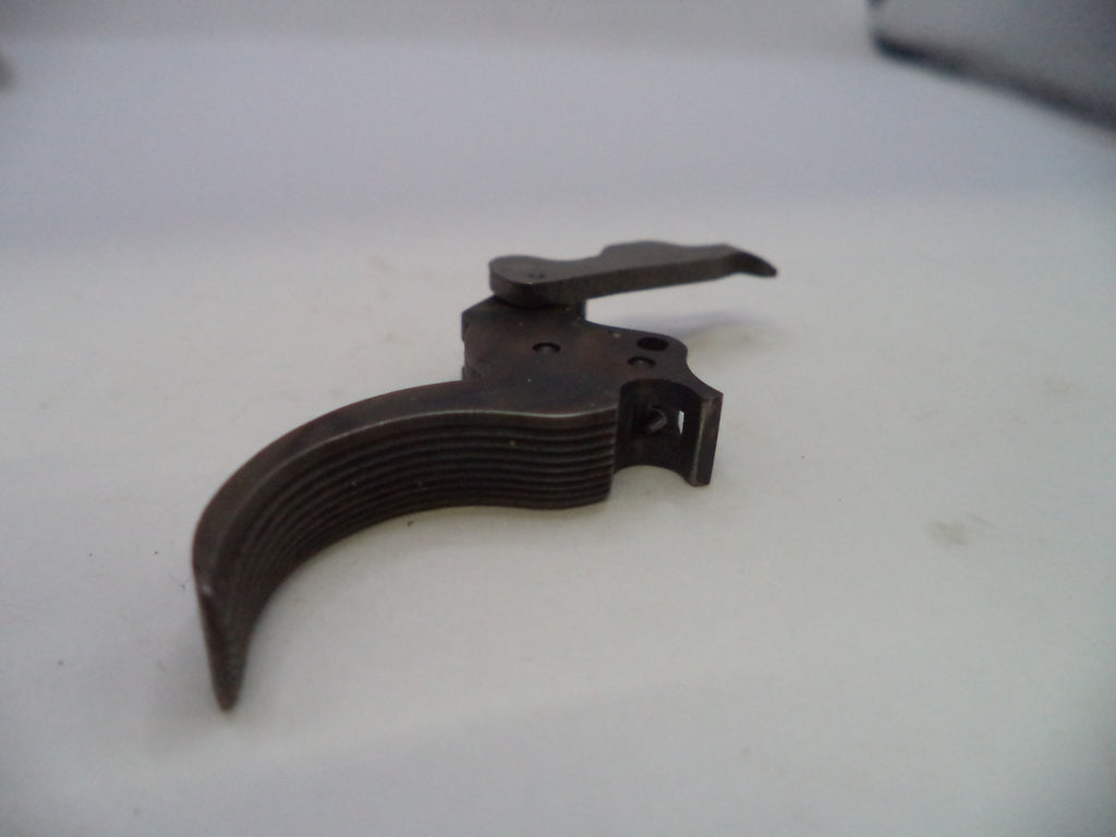 A dark metal replacement trigger component for a firearm, photographed on a plain off-white surface.
